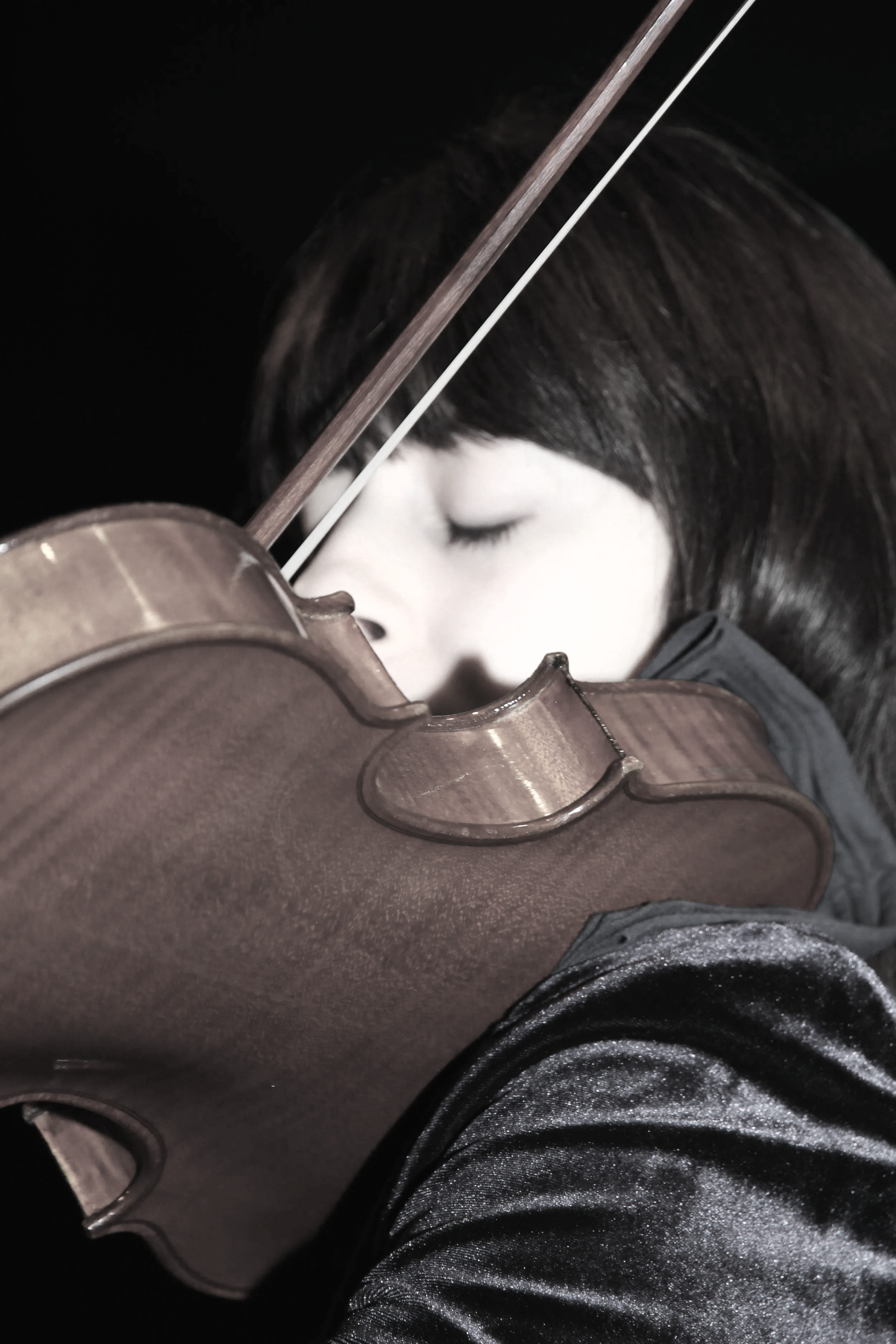 A woman with dark hair playing a violin, with eyes closed and a peaceful expression.