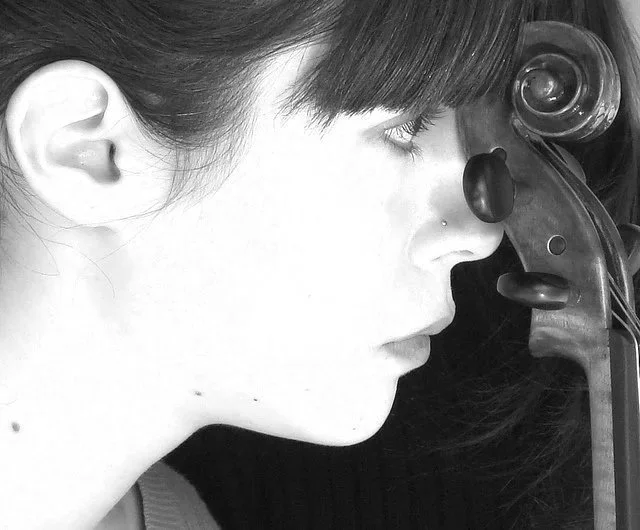A close up of a woman with dark hair and a nose piercing looking at her violin.