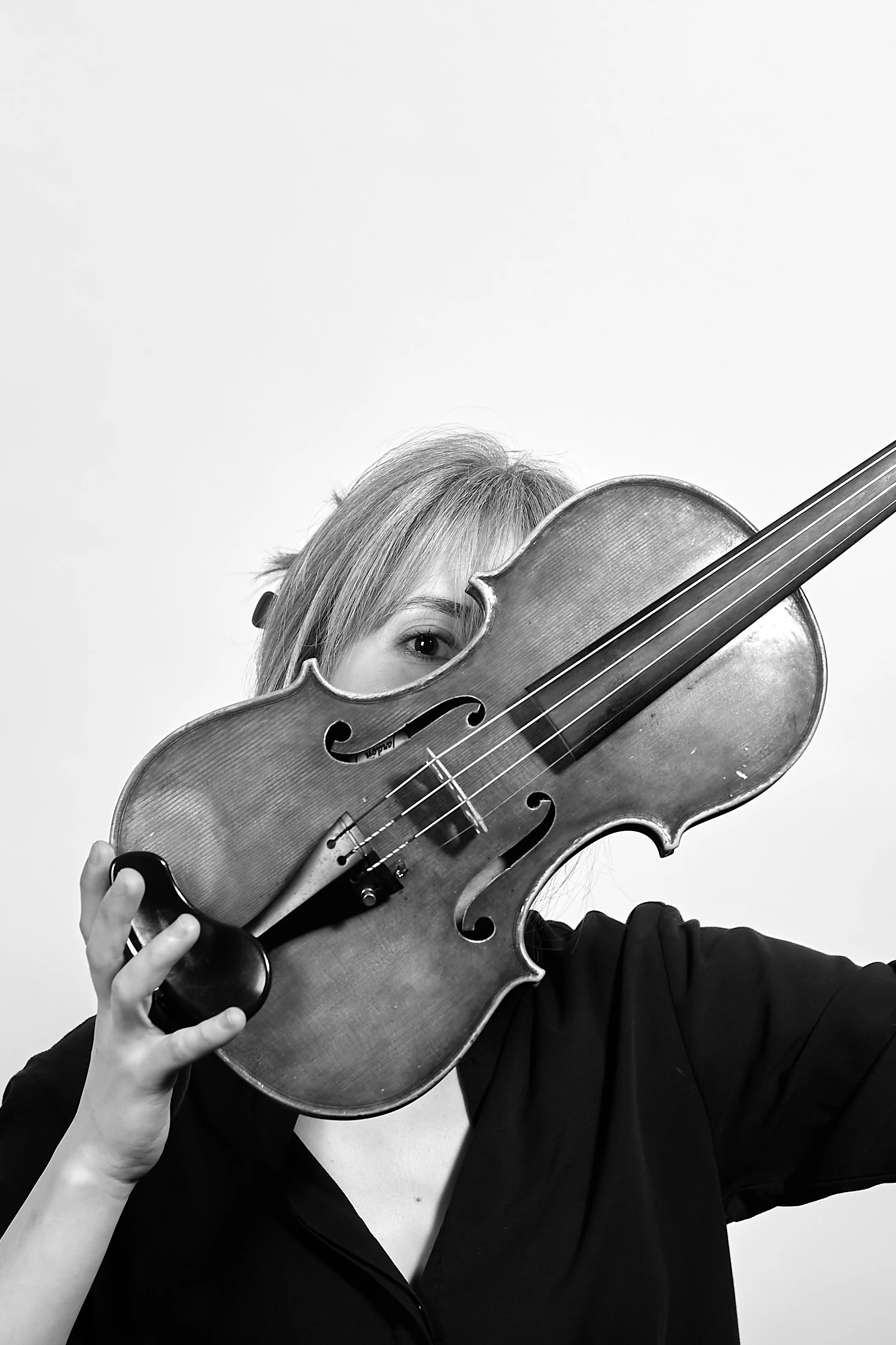 A woman, Talia Ramos, holding a violin to her face, with one eye visible over it, in black and white.