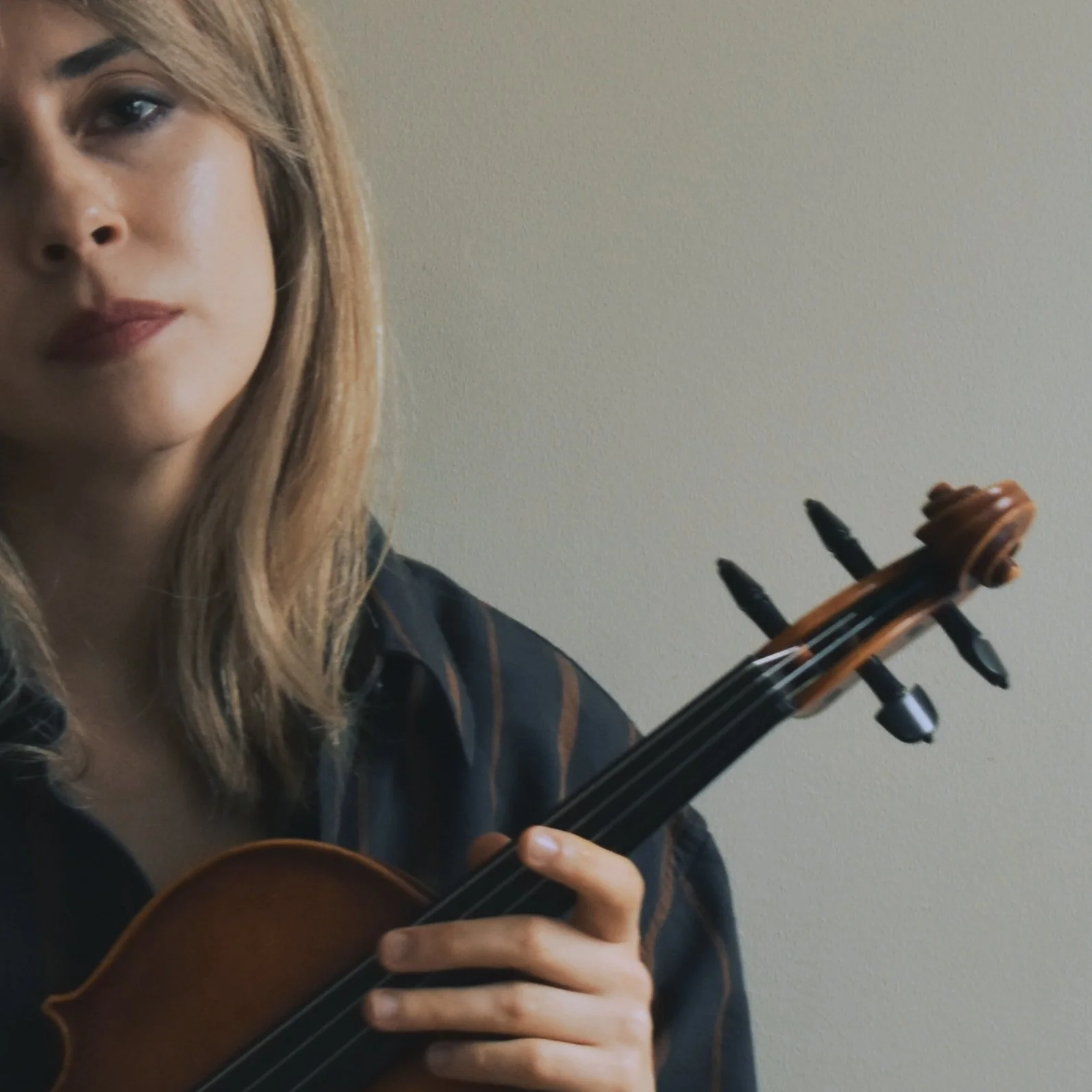A close up of a woman holding her violin and looking directly at the camera.