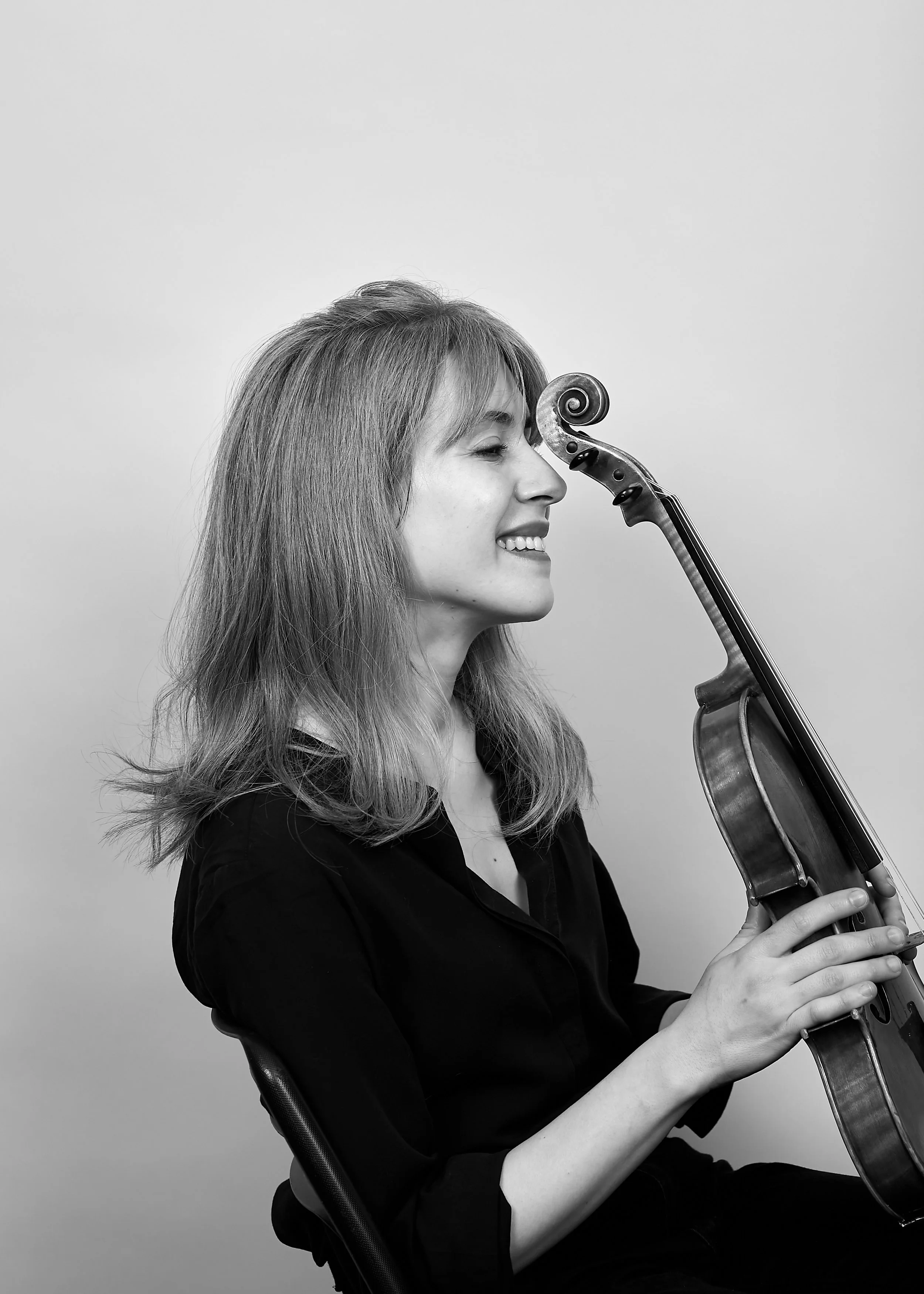 A woman, Talia Ramos, smiling and sitting with a violin near her face, in black and white.