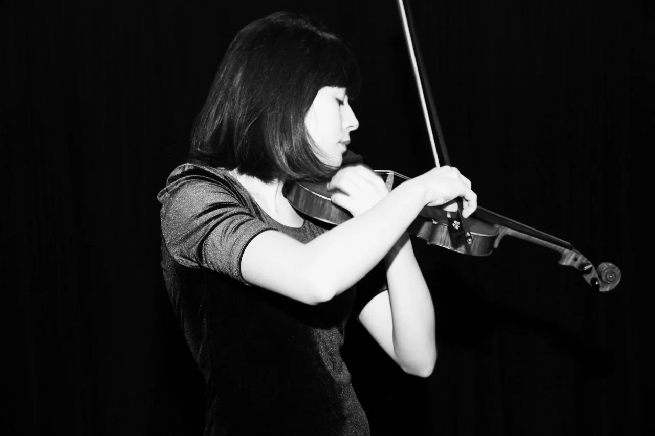 A woman, Talia Ramos, with shoulder-length hair playing the violin in a black-and-white photo.