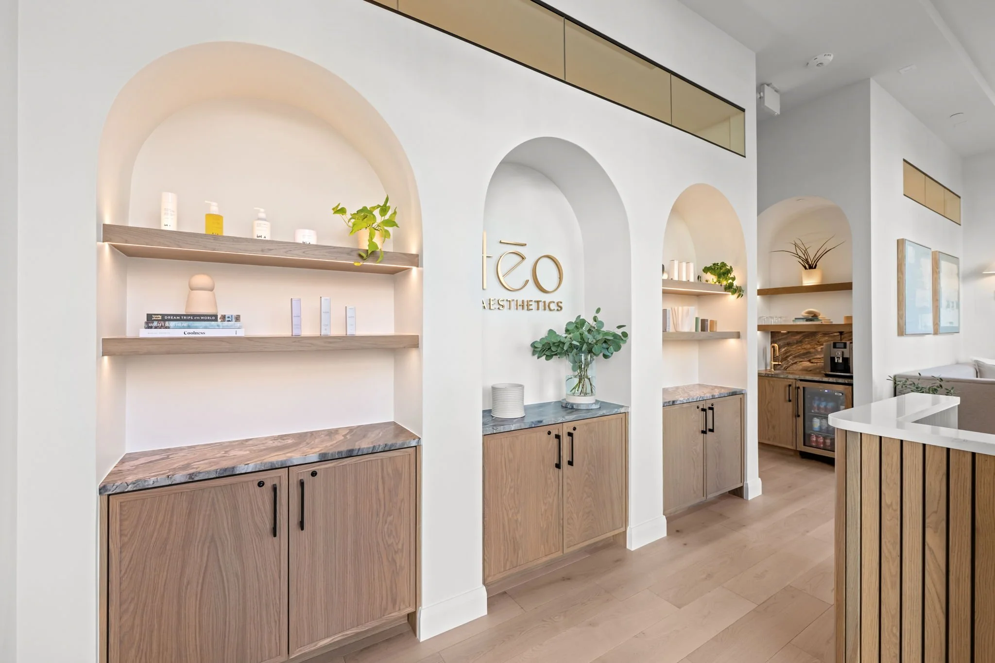 Interior of a modern aesthetic clinic with wooden cabinets, decorative shelves, and a minimalistic design. The logo 'téo AESTHETICS' is displayed on the wall.