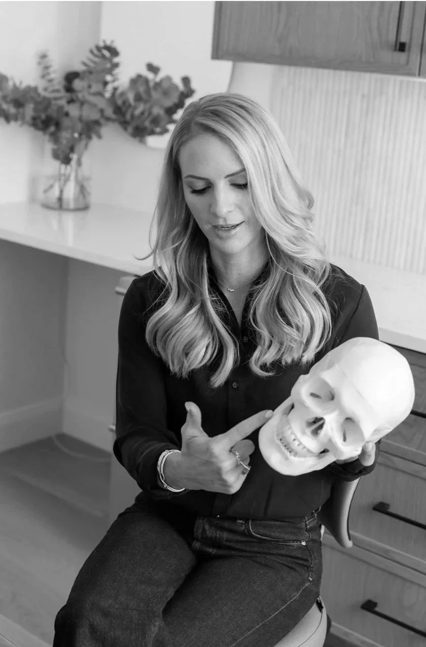 A woman with long, wavy hair holding a human skull and pointing at it with her finger.