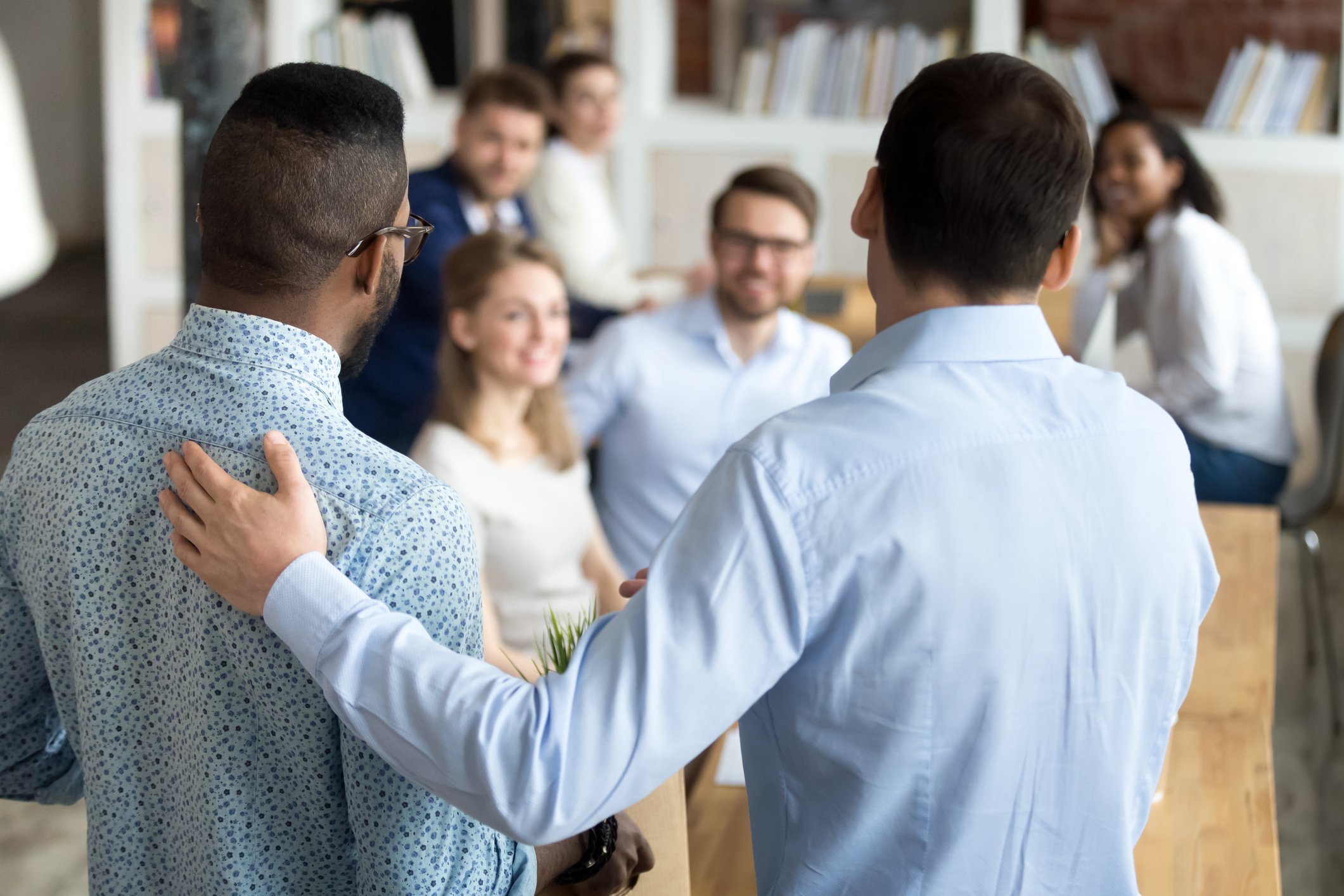 Two men speaking to a group of diverse people in a professional setting, possibly a workshop or seminar.