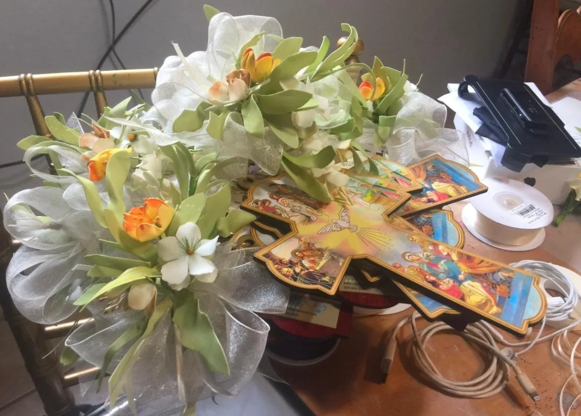 A table with a floral arrangement, religious cards, and various office supplies including cords and tape.