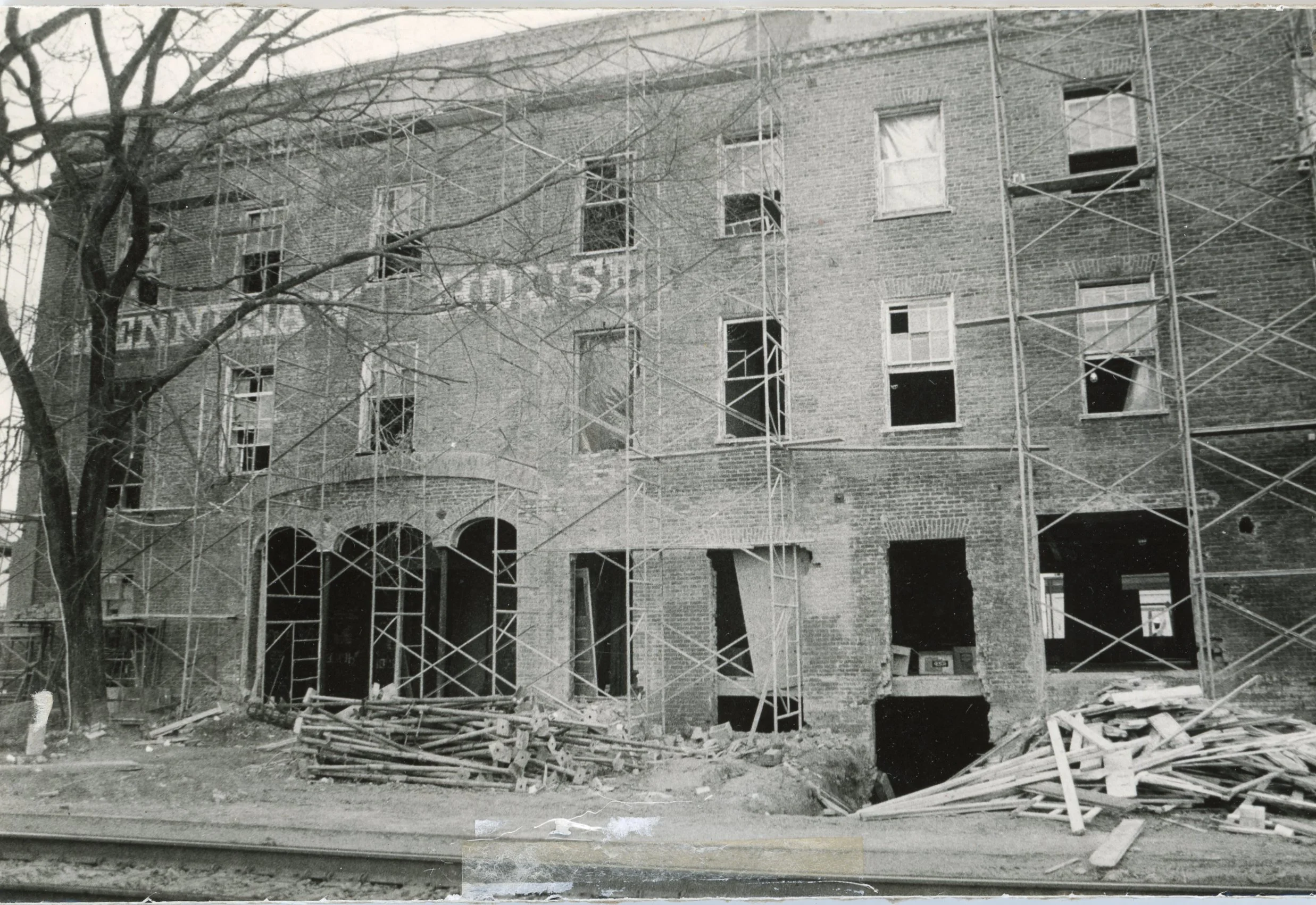 Black and white photo of a multi-story brick building under construction, with scaffolding surrounding it and open window frames.
