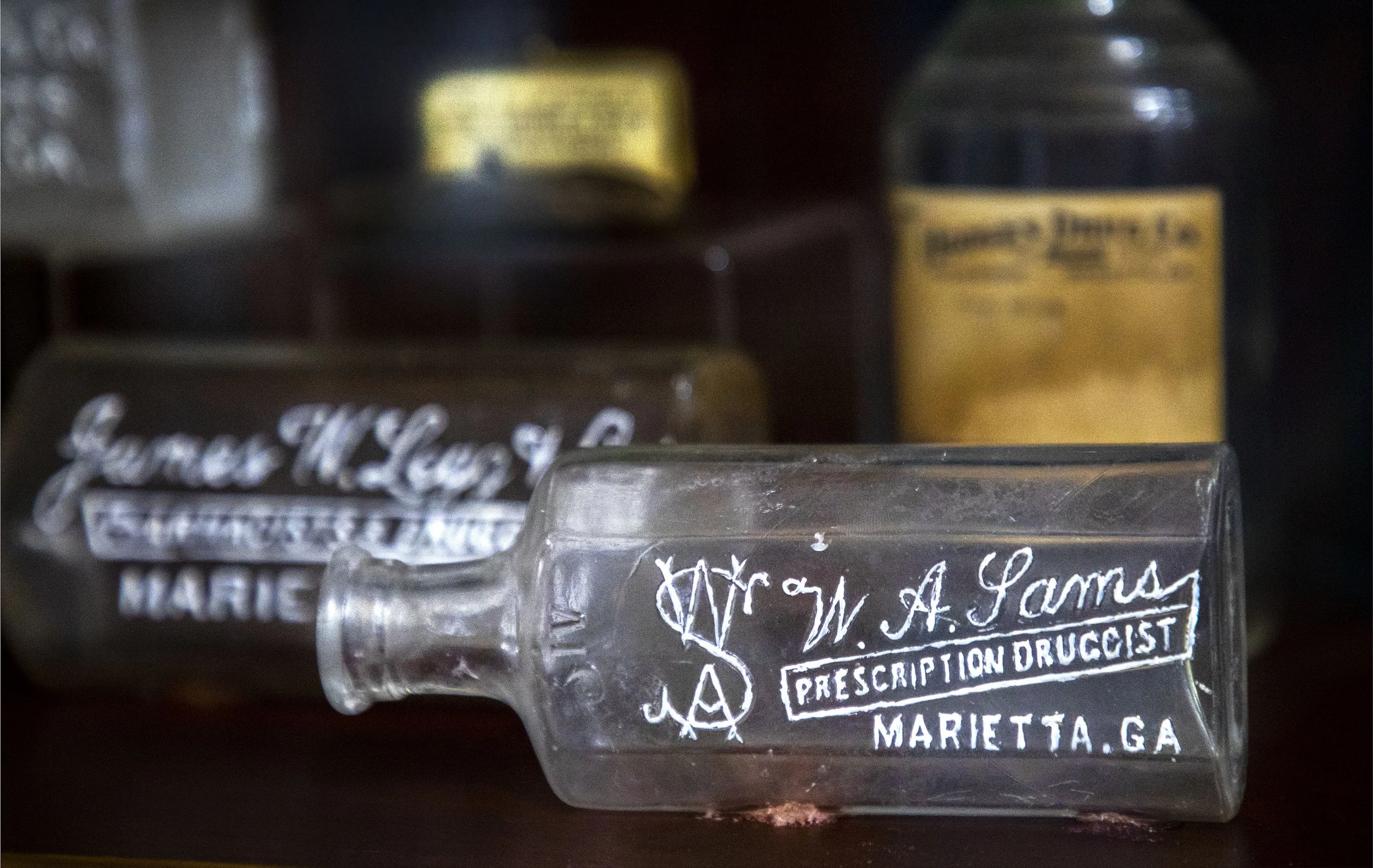 Close-up of glass bottles with painted raised lettering for the pharmacy they came from.