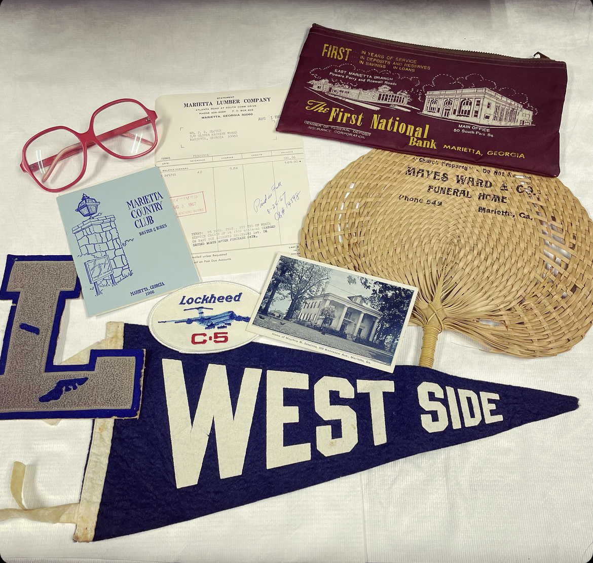 Collection of vintage memorabilia including a maroon bank cover, woven fan with business info, black and white photo of a house, blue Marietta Country Club card, gray and blue patch with "T-1" and a dog silhouette, Lockheed -5 patch, pink glasses, receipt, and a navy blue "WEST SIDE" pennant.