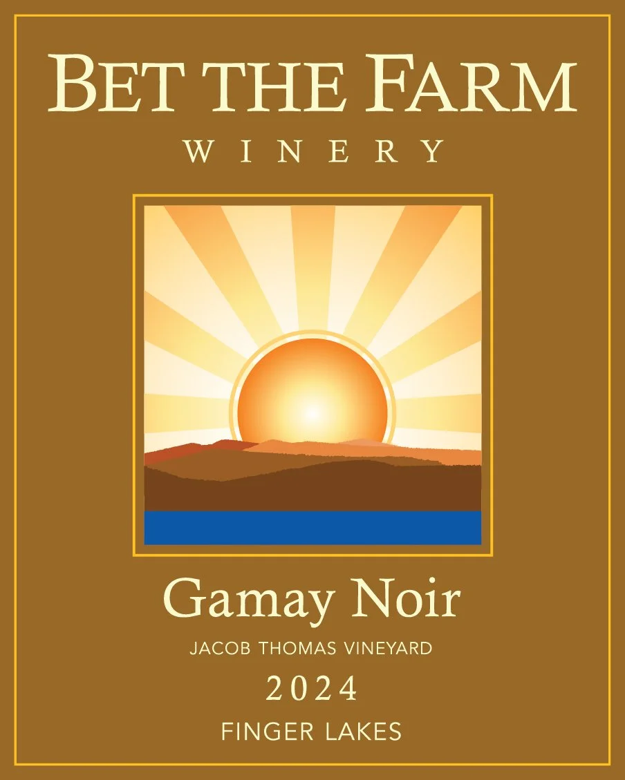 The image shows a wine label for Bet the Farm winery. The label features a stylized sunset or sunrise over a landscape, with rays emanating from the sun. The text on the label reads: 'Bet the Farm Winery,' 'Gamay Noir,' 'Jacob Thomas Vineyard,' '2024,' and 'Finger Lakes.' The background color of the label is brown with a gold border.