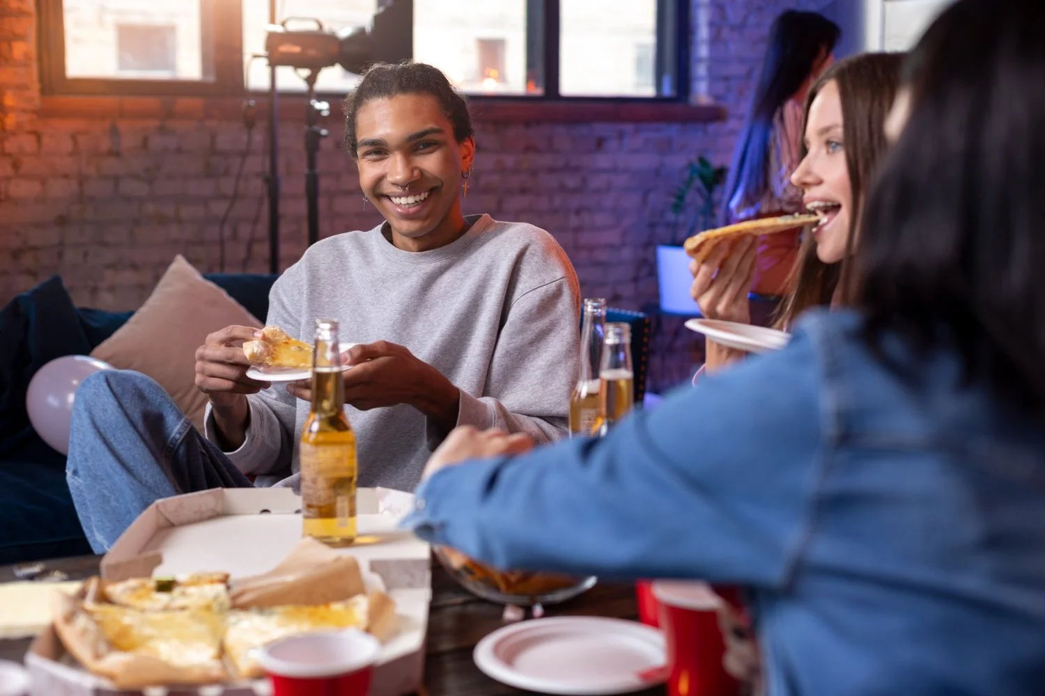 Group of friends enjoying pizza and drinks at a casual indoor gathering.