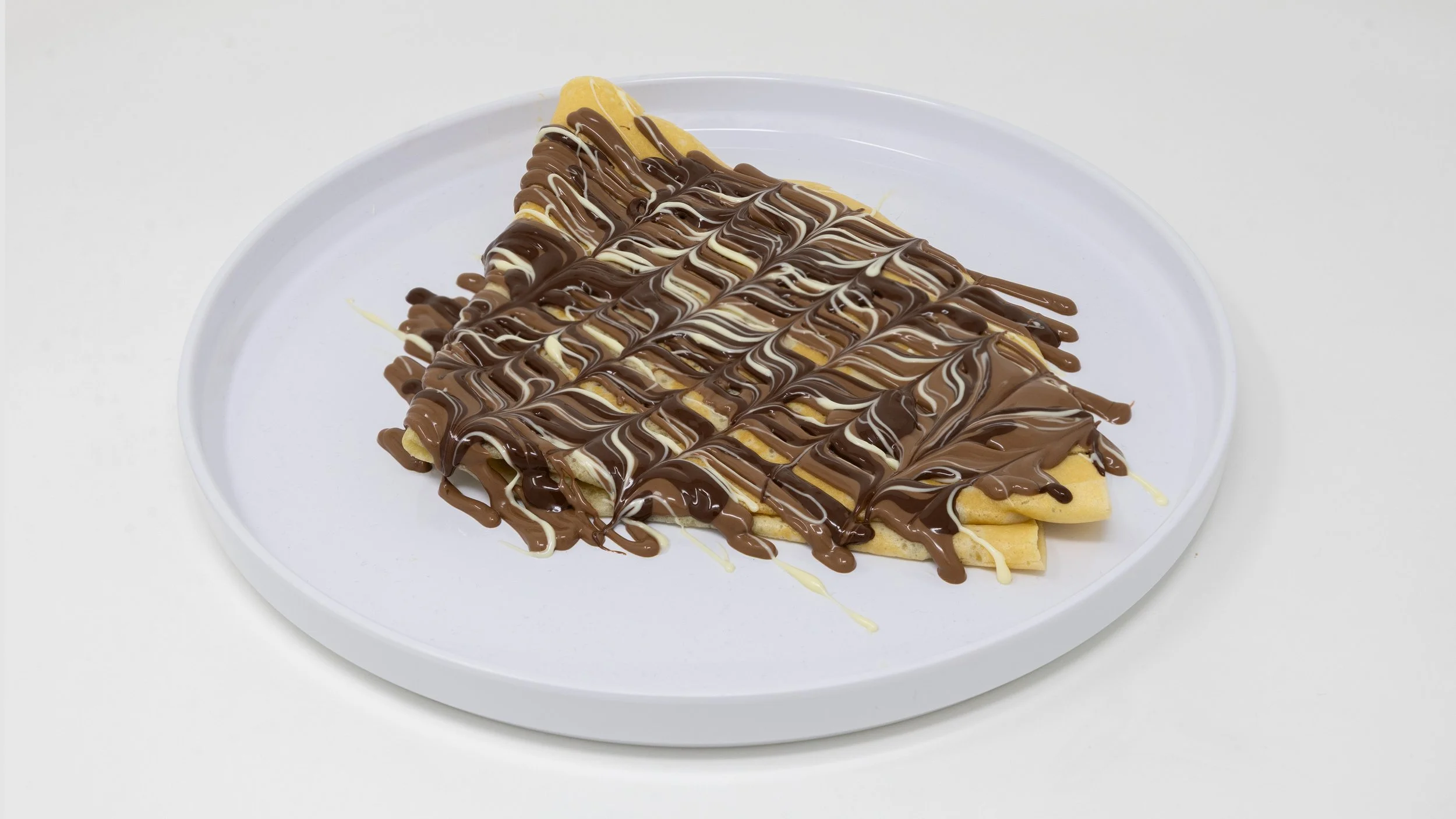 A waffle folded in half and topped with drizzles of milk, white, and dark chocolate on a white plate.