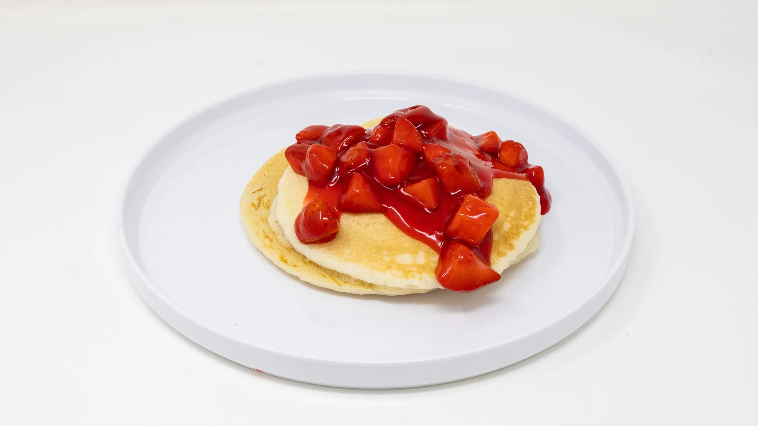 Pancakes topped with strawberry syrup and fruit on a white plate.