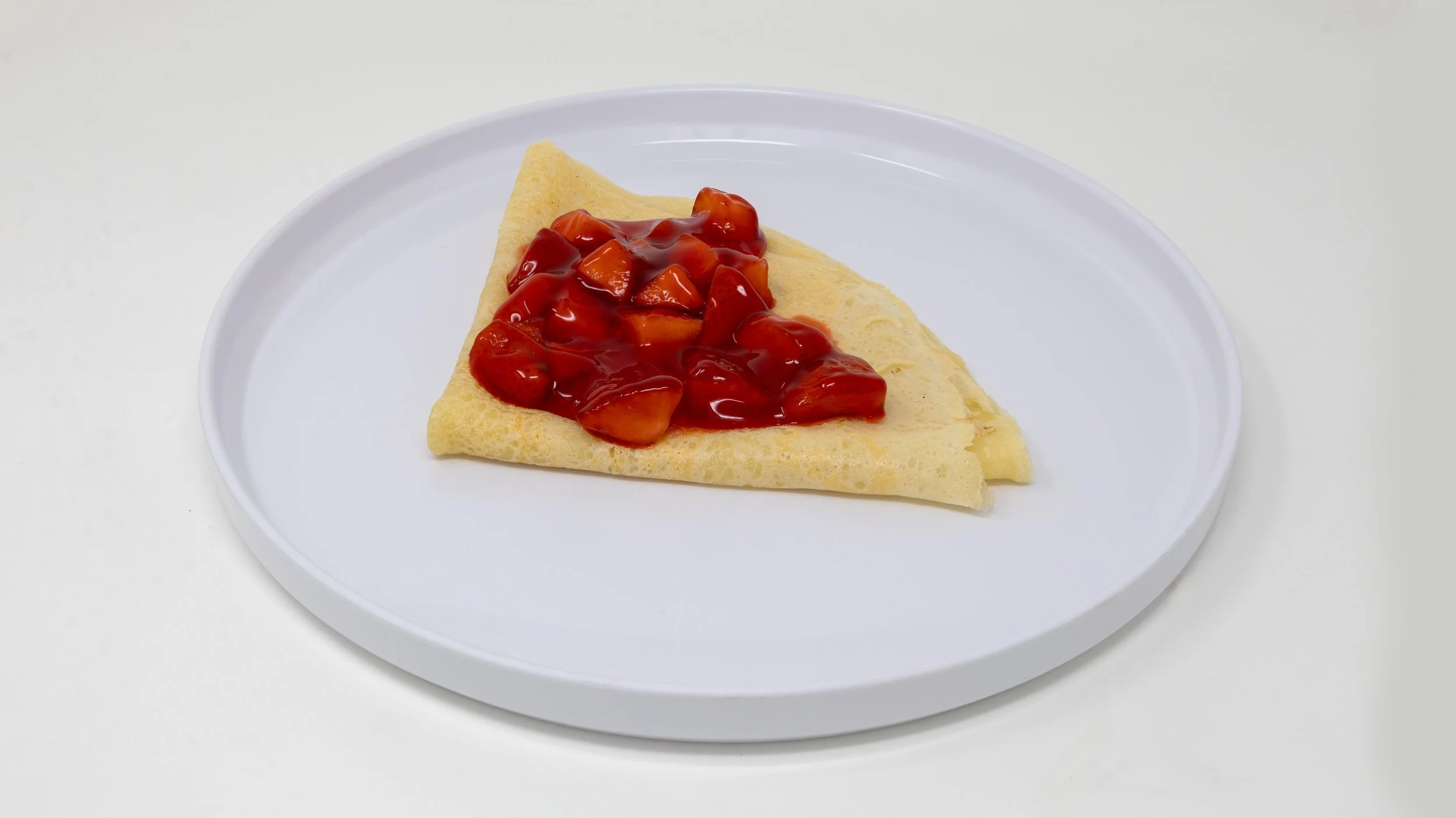 A single crepe folded into a triangle on a white plate, topped with strawberry and peach fruit compote in red sauce.