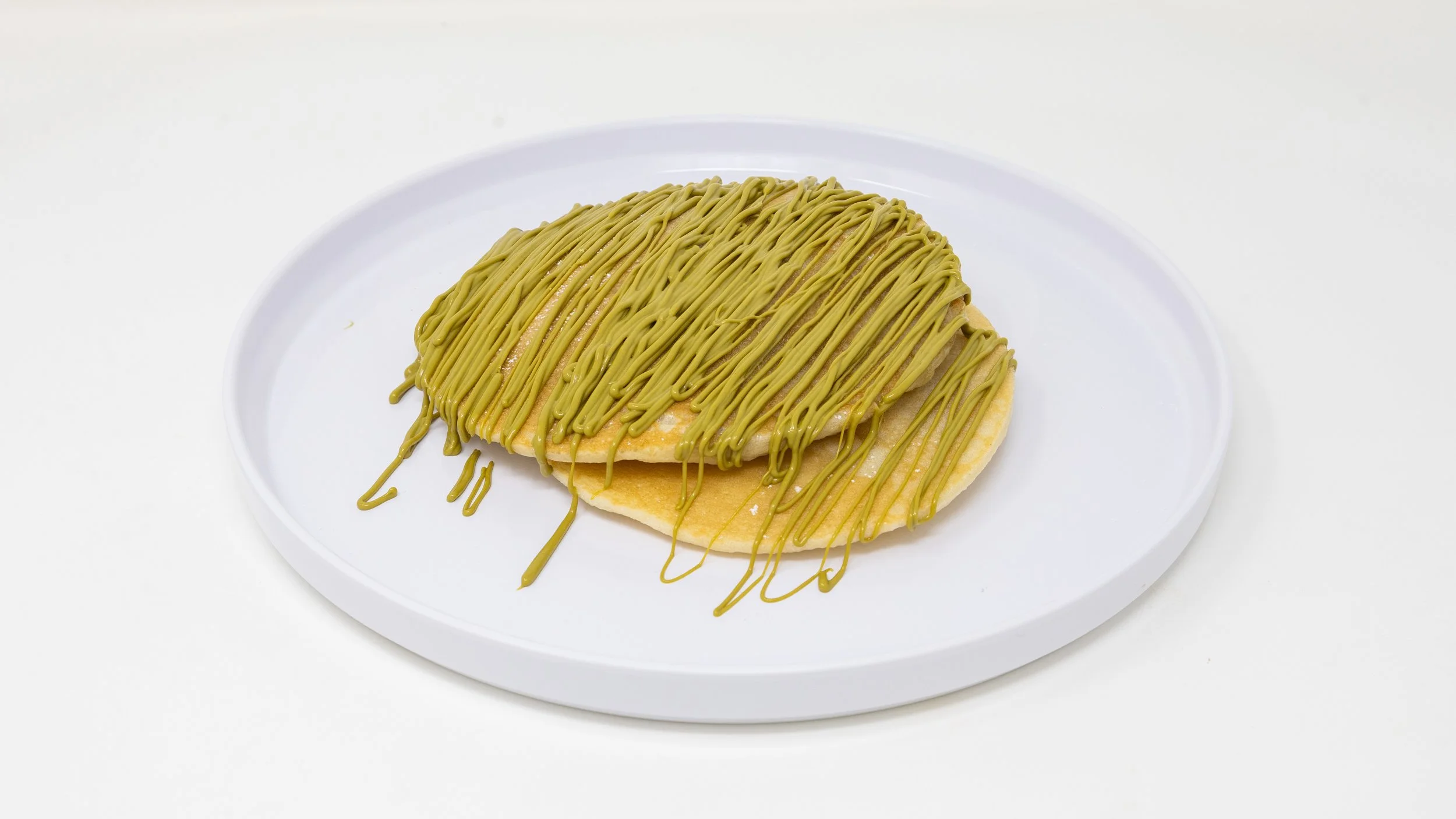A slice of bread topped with a yellow spread and drizzled with green matcha-flavored icing on a white plate.