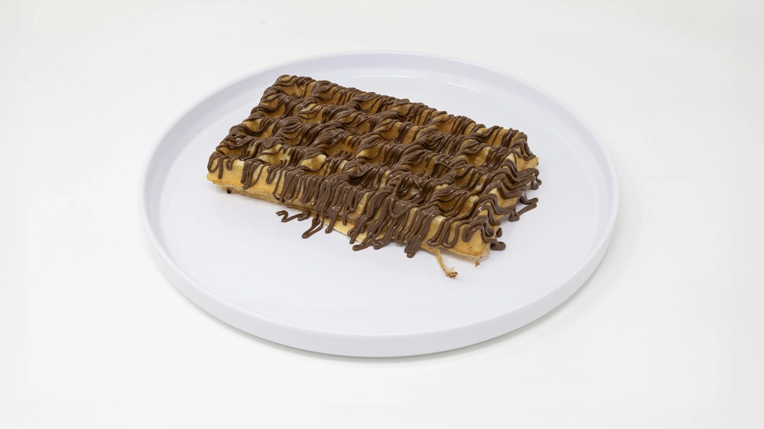 A rectangular waffle drizzled with chocolate sauce on a white plate against a plain white background.