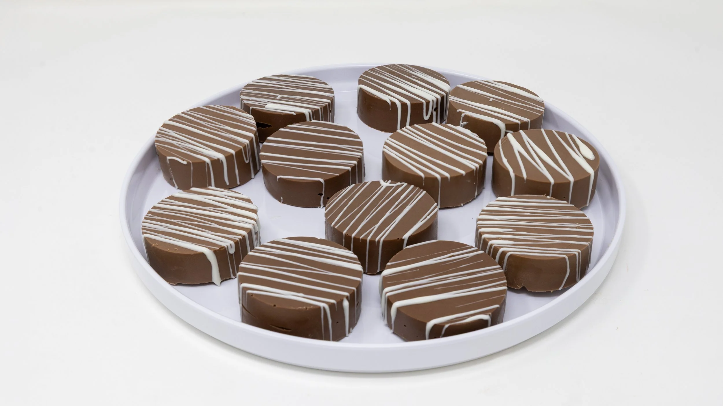 Assorted round chocolates with white drizzle on a white tray.