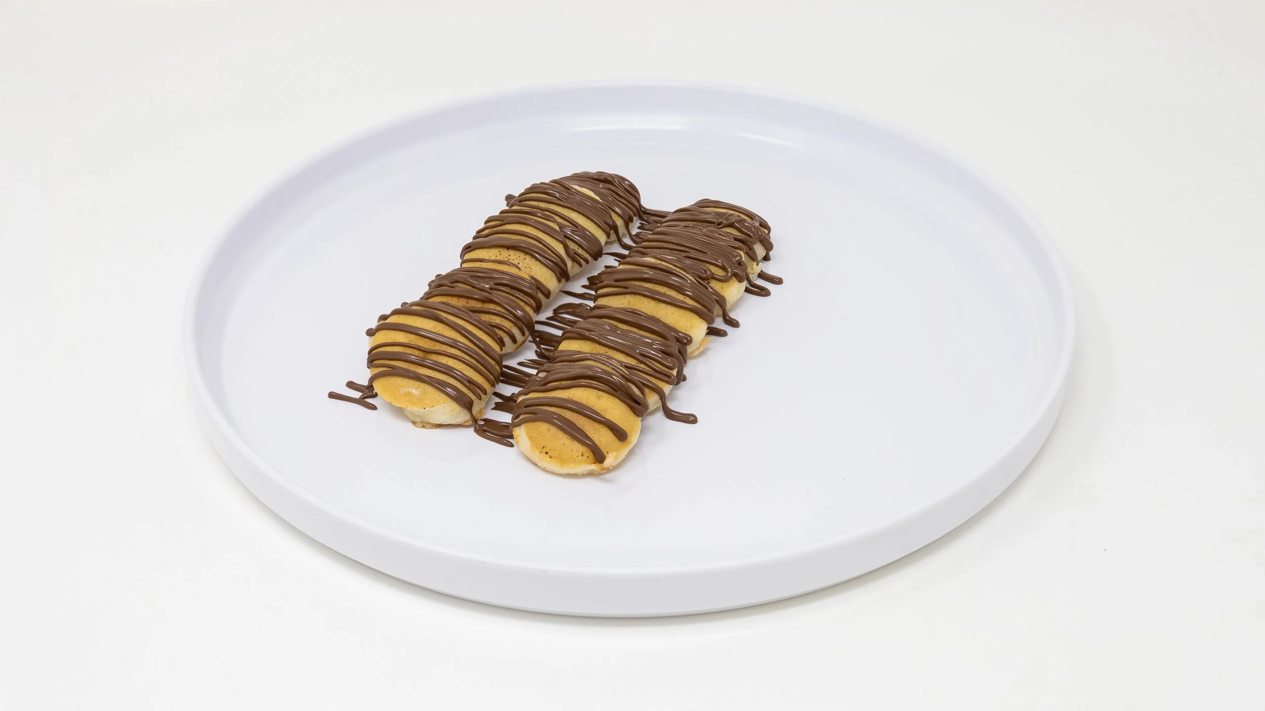 Three banana split éclairs drizzled with chocolate on a white plate.
