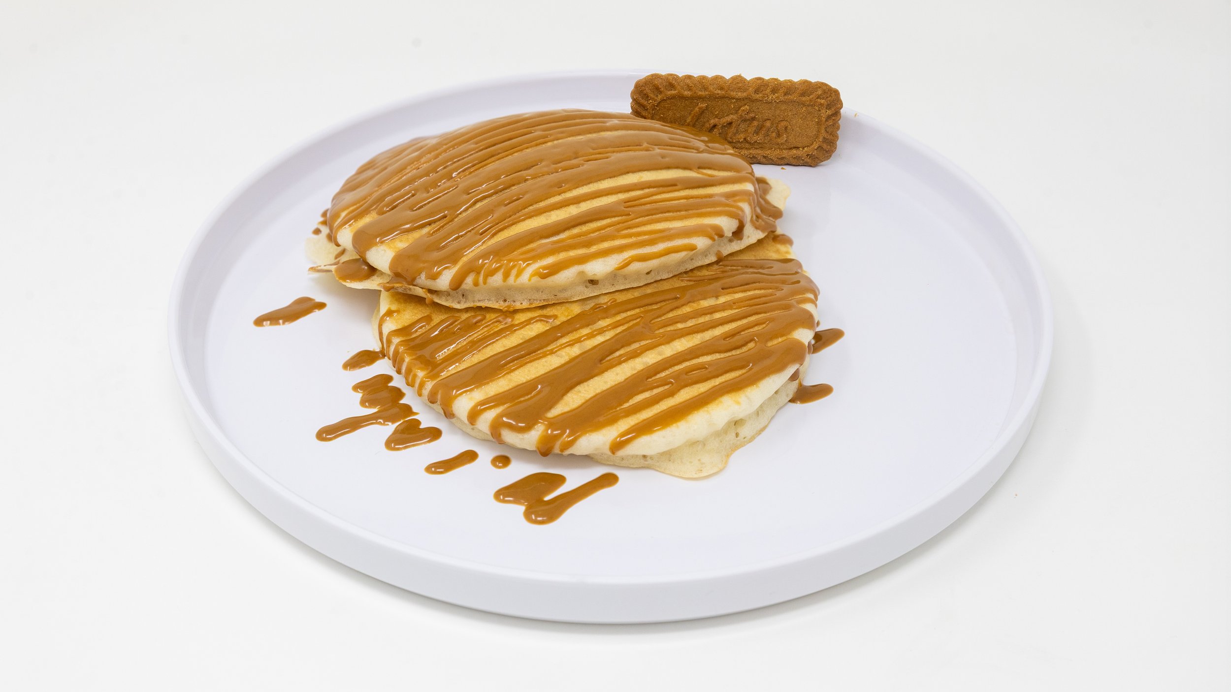 Two pancakes topped with caramel sauce on a white plate, with a Lotus biscuit.