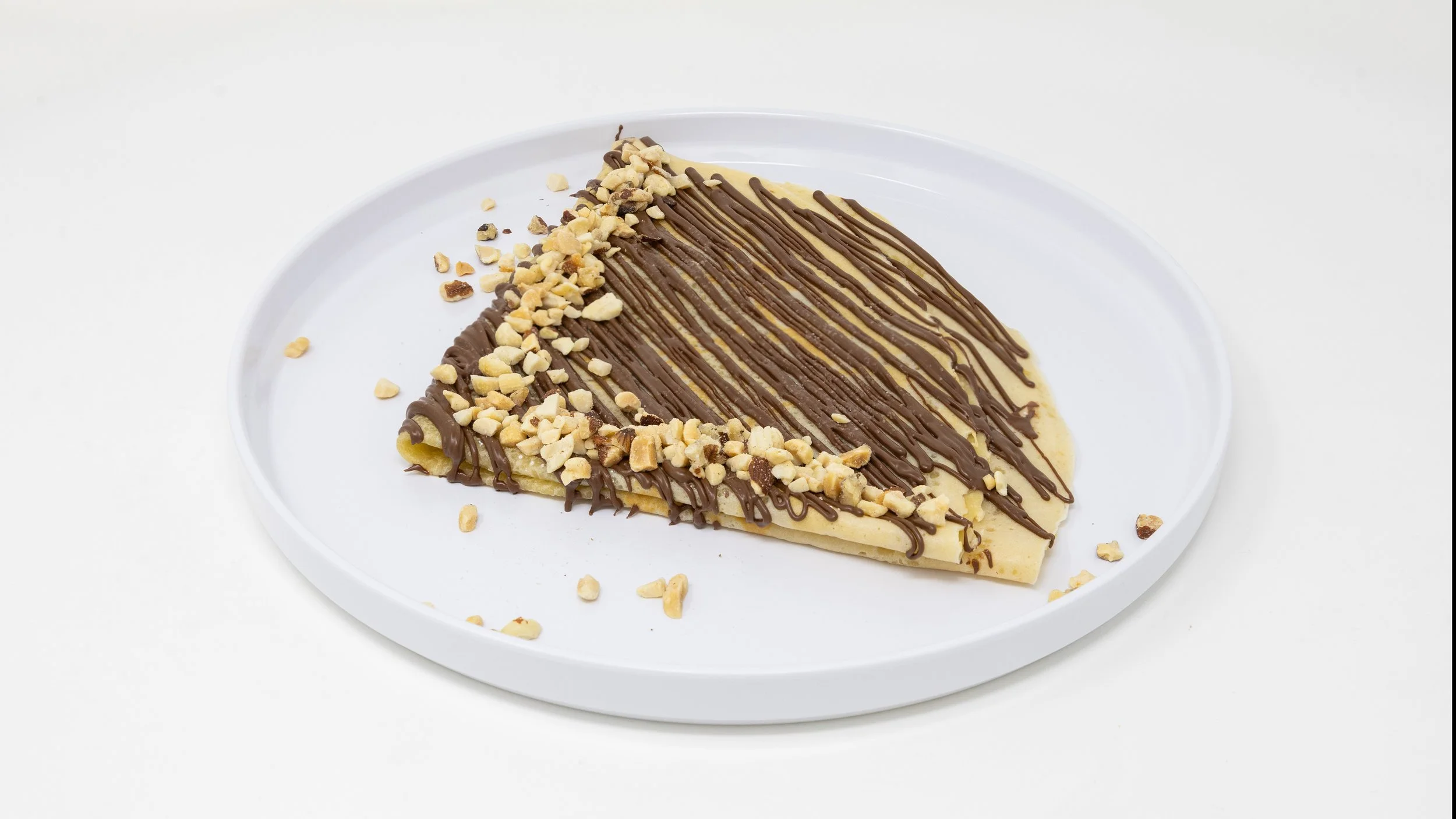 Slice of creamy dessert topped with chocolate drizzle and chopped nuts on a white plate.