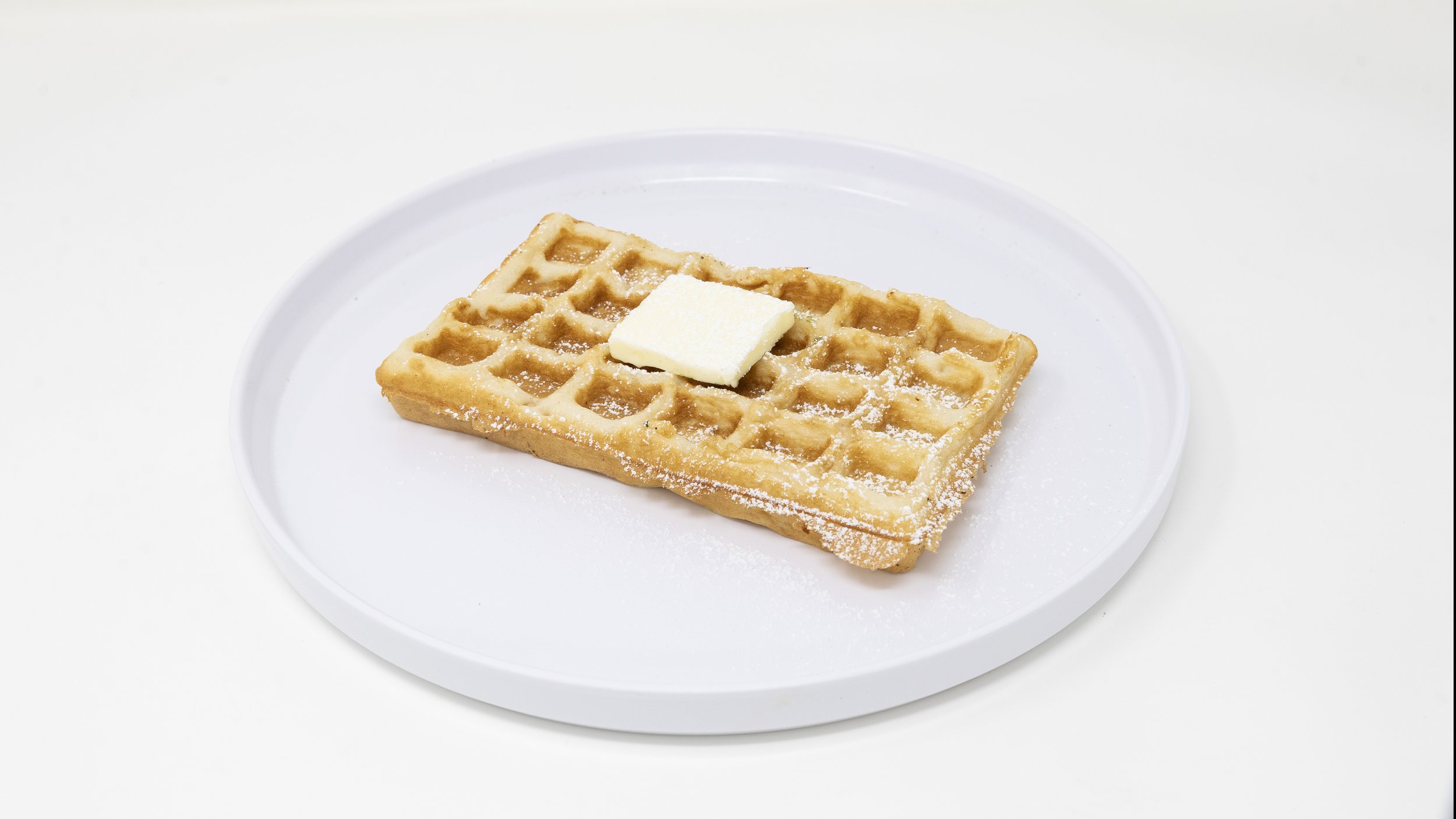 A rectangular waffle topped with a pat of butter and powdered sugar on a white plate.