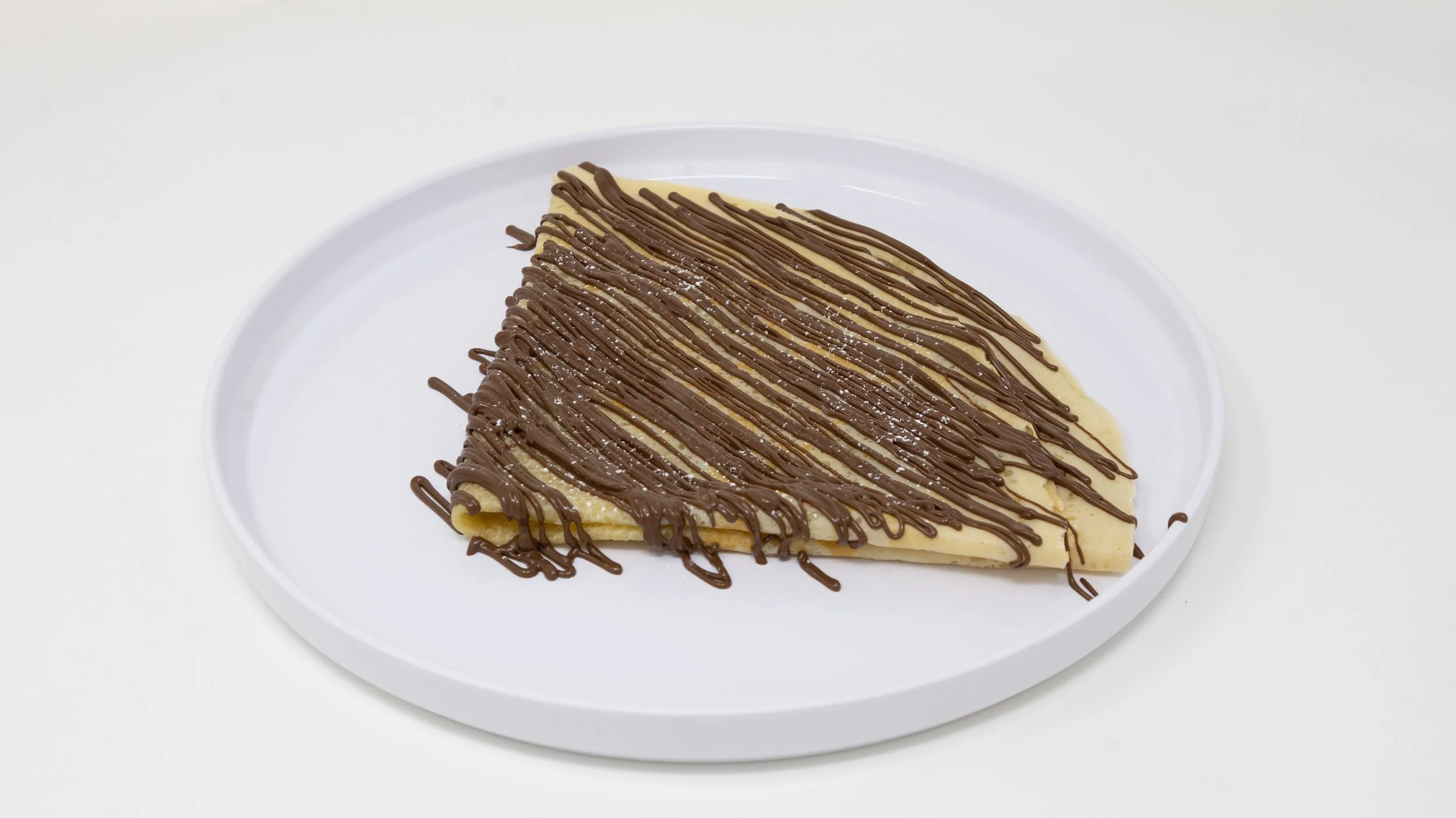 Slice of crepe with chocolate drizzle on a white plate.