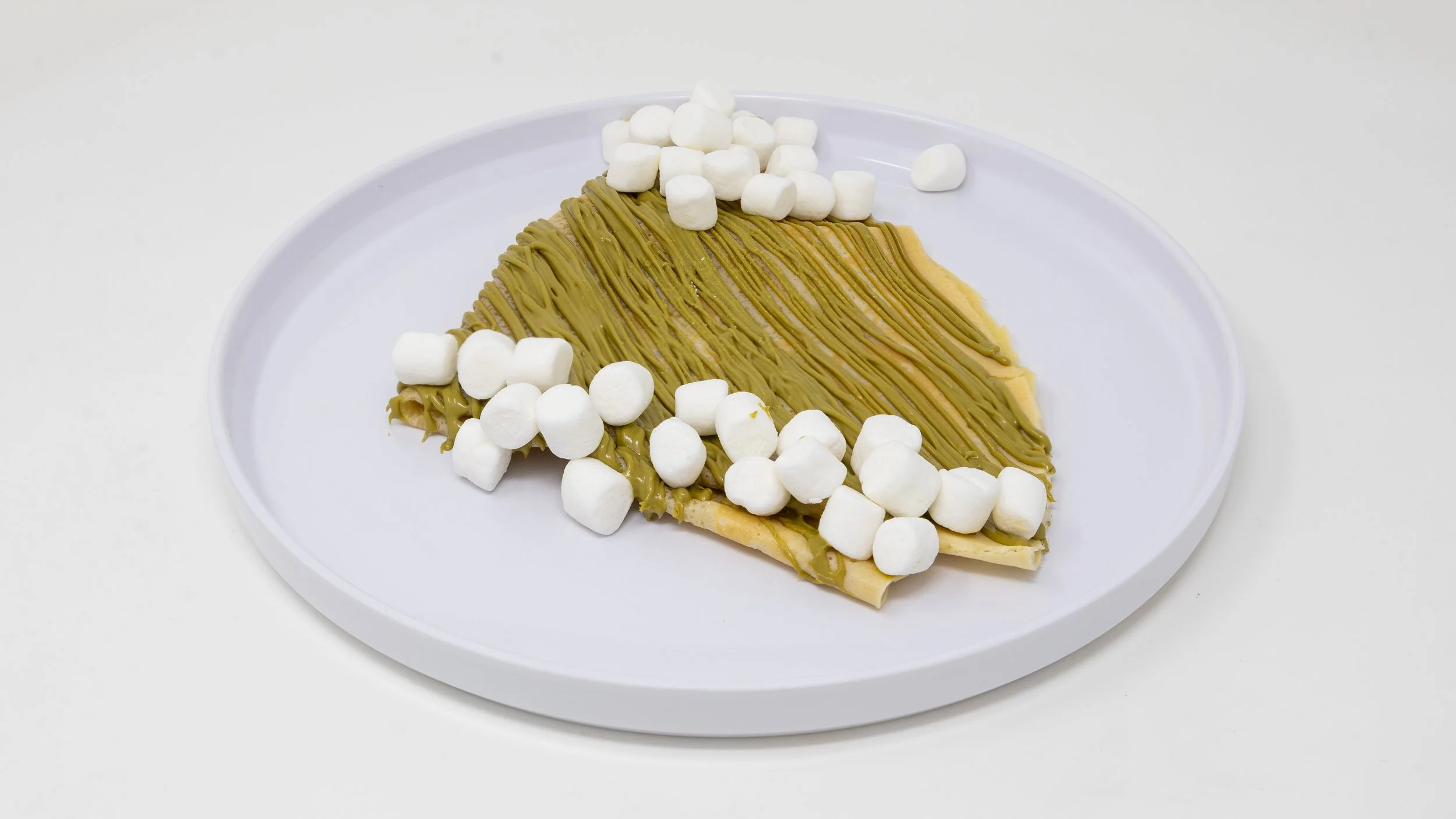 A slice of cake with greenish-brown frosting, topped with white mini marshmallows, on a white oval plate.