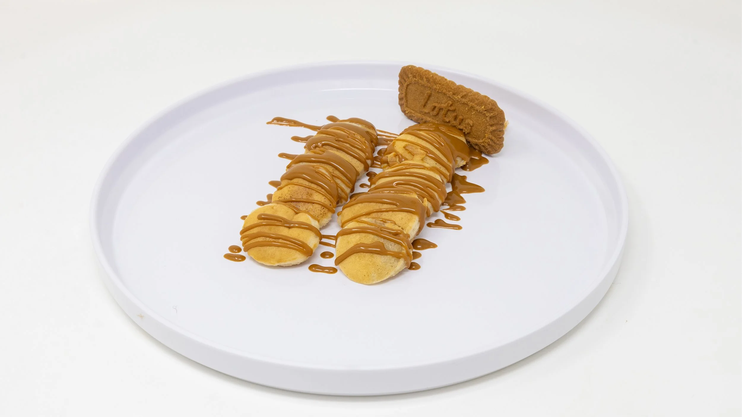 Two banana slices drizzled with caramel sauce and a graham cracker rectangle on a white plate.