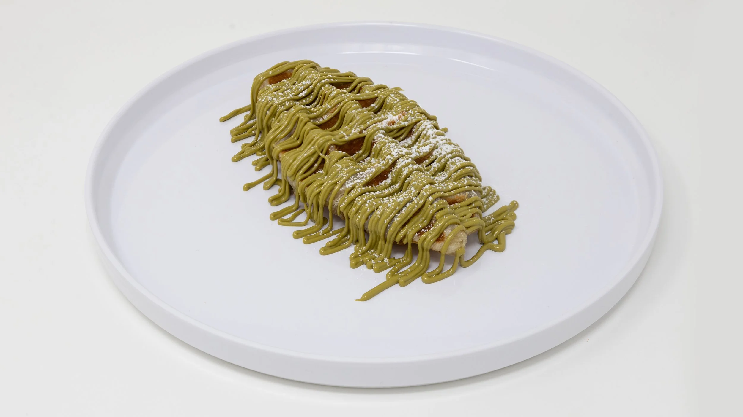 A banana split topped with green matcha drizzle and powdered sugar on a white plate.