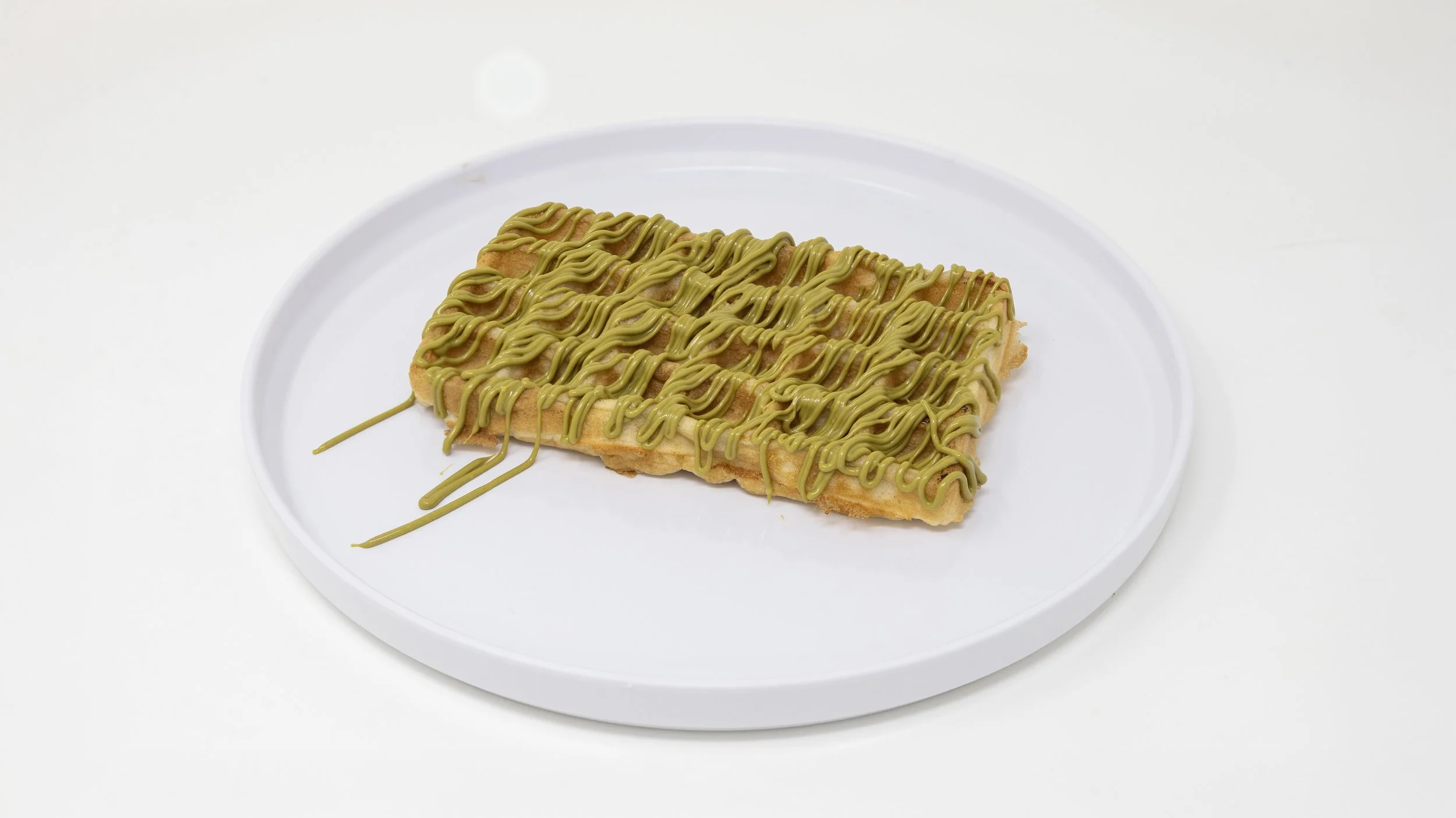 Waffle topped with green matcha-flavored icing drizzled over it, served on a white plate.