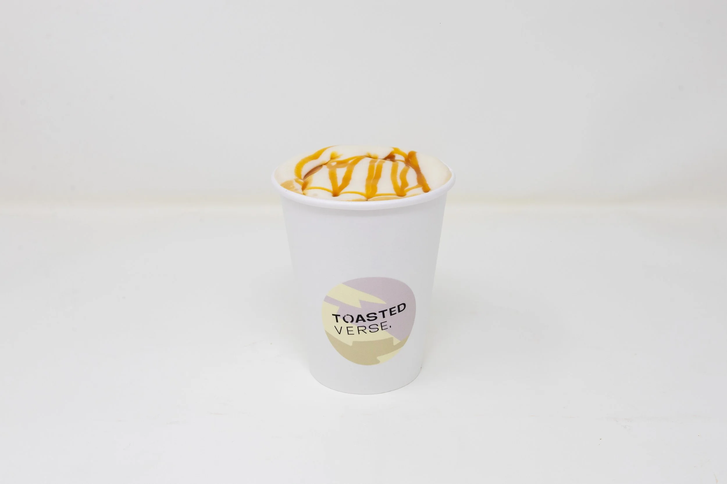 A cup of vanilla ice cream with caramel drizzle on top, in a white paper cup with a "Toasted Verse" label, against a plain white background.