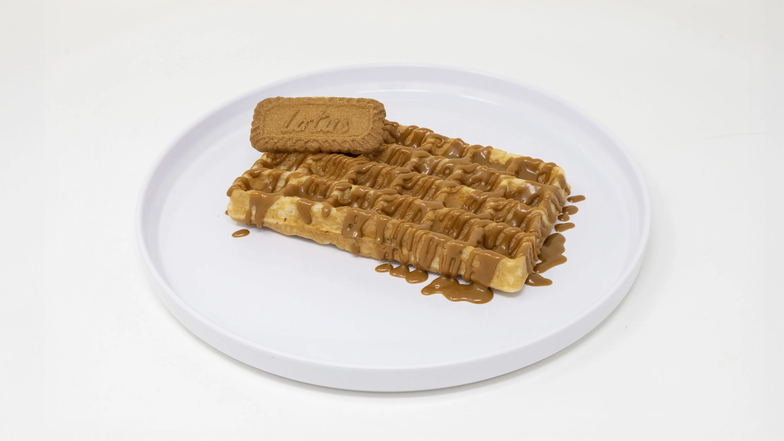A white plate with two waffles topped with caramel sauce and a rectangular biscuit on top.