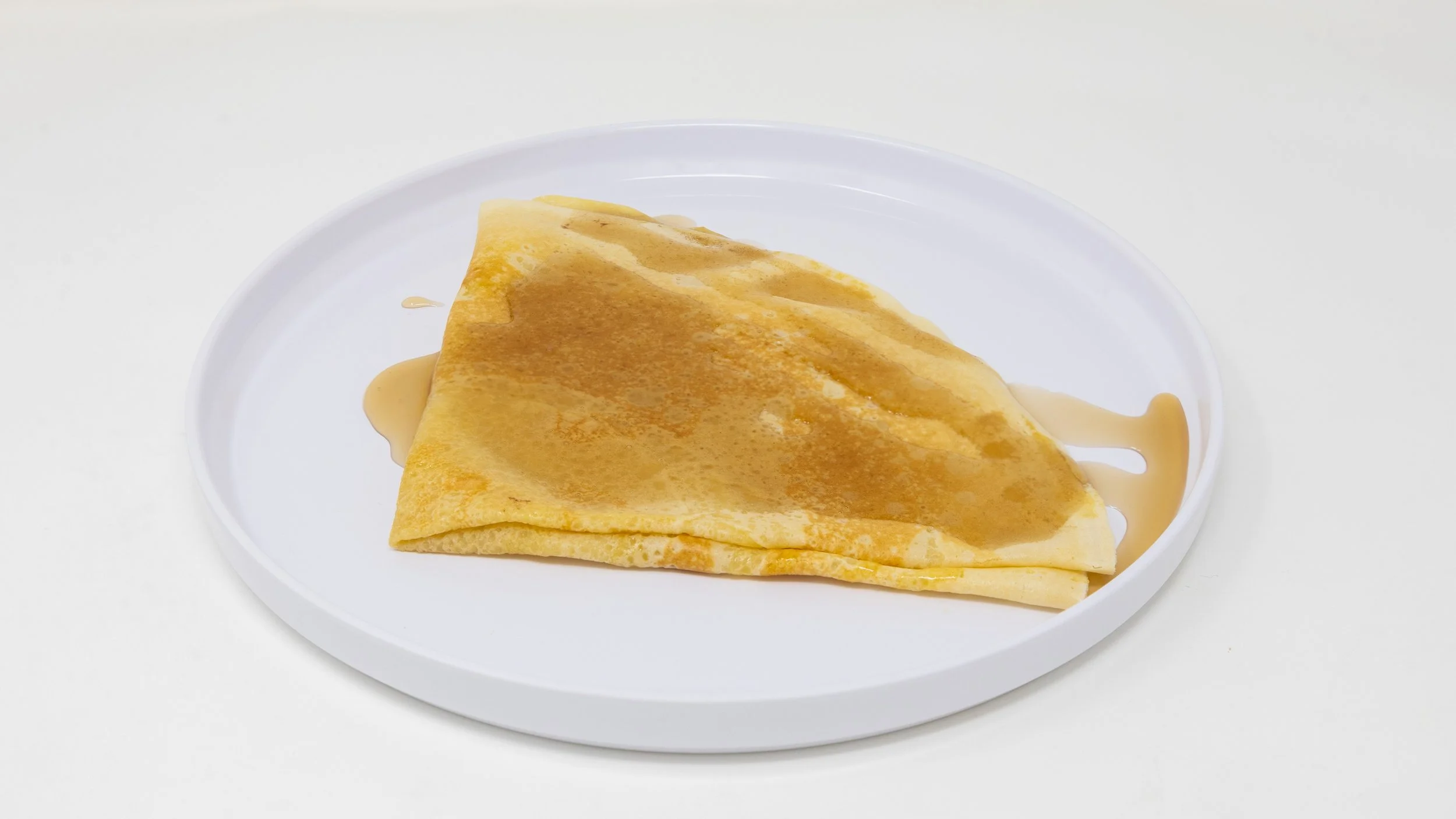 Crepe folded in half on a white plate, topped with syrup.