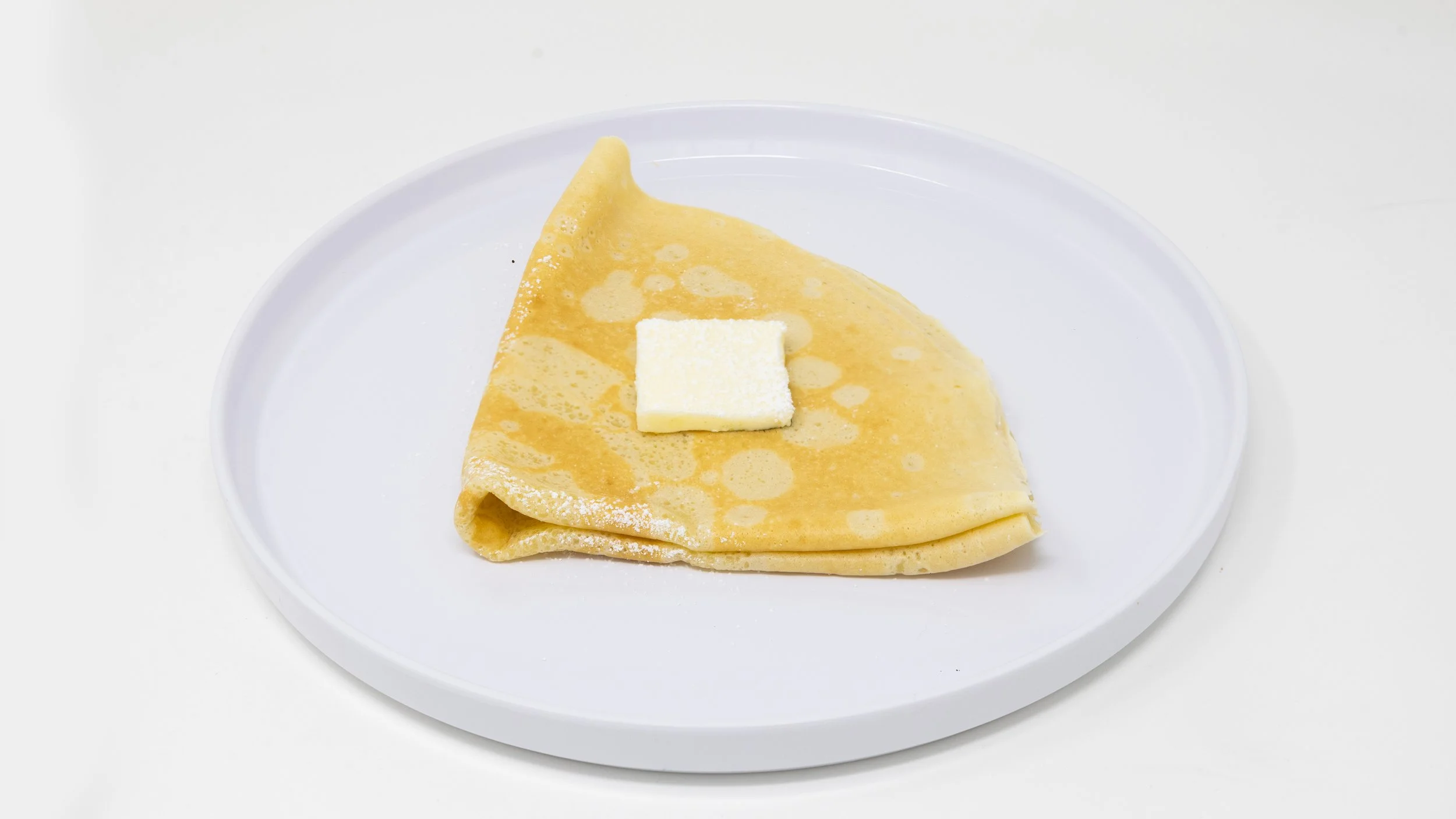 A crepe folded into a cone shape on a white plate with a pat of butter on top.
