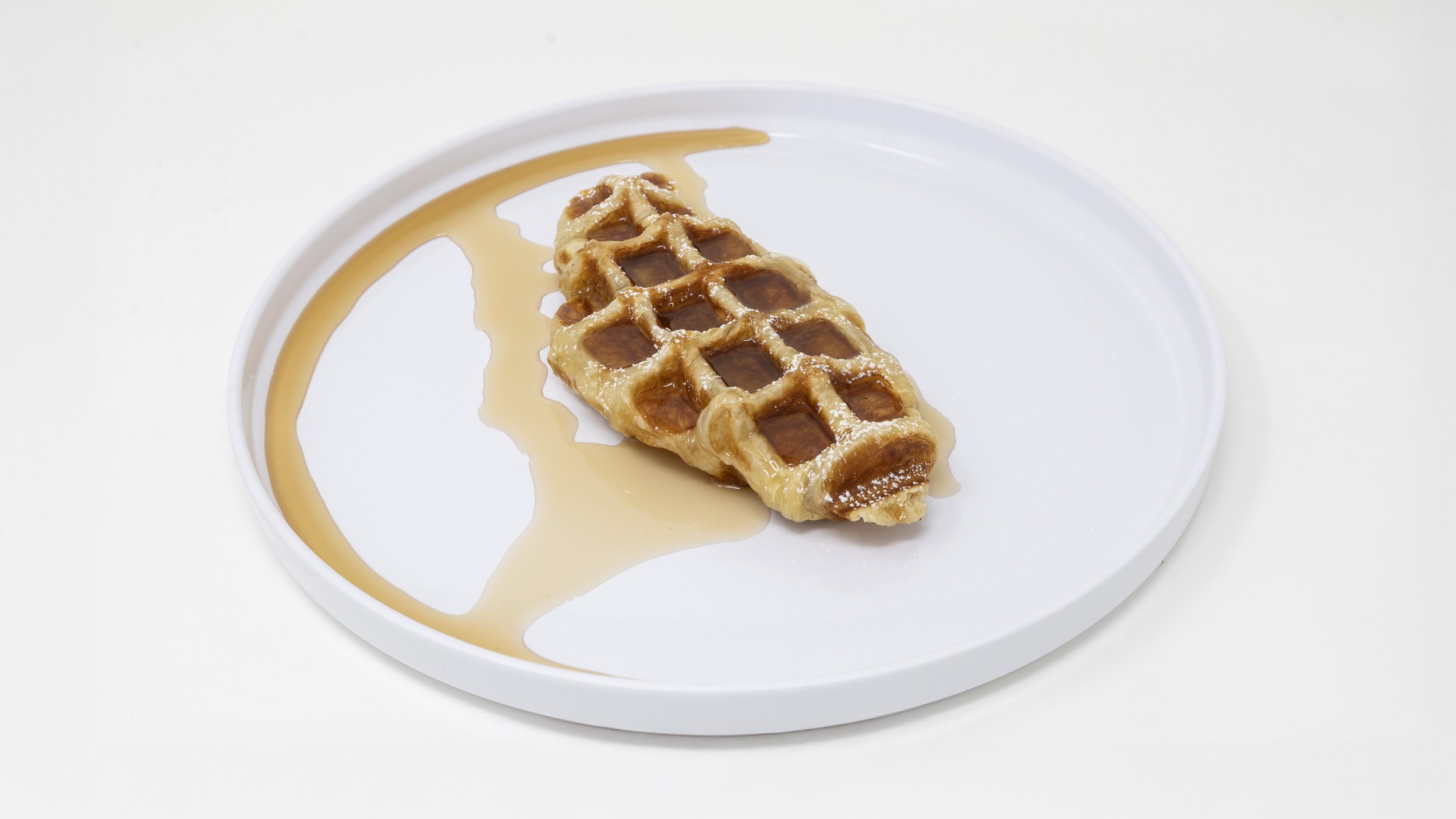 A partially eaten waffle with syrup on a white round plate.