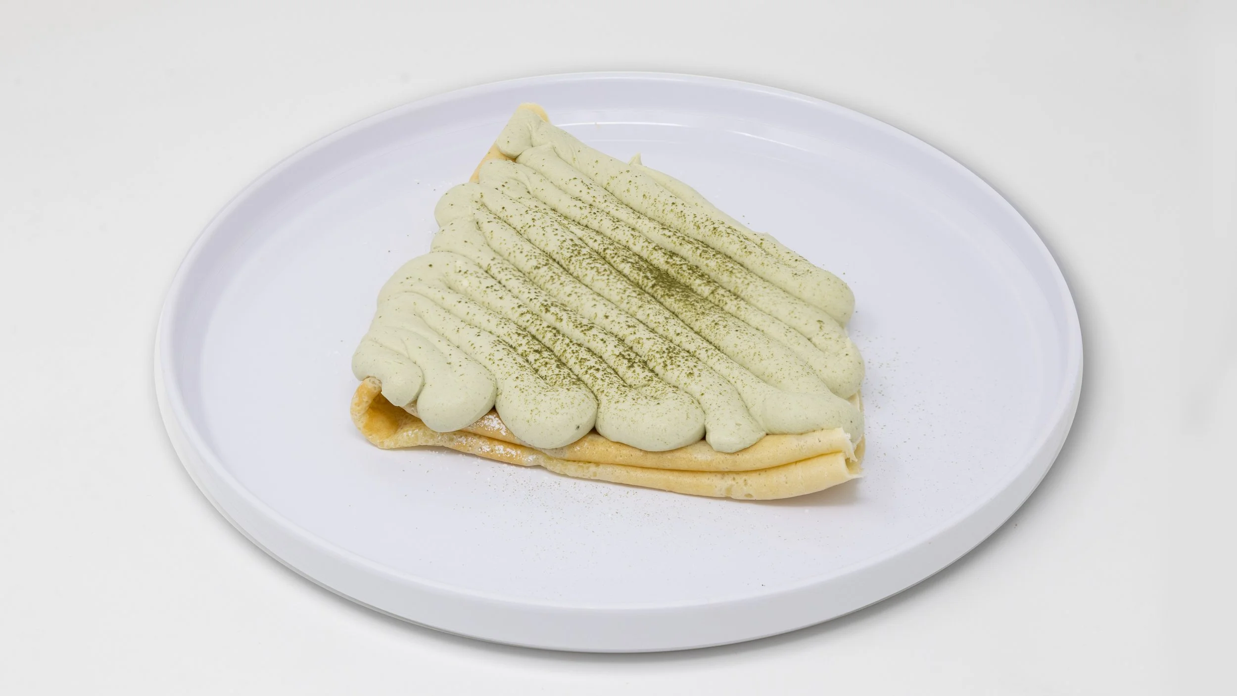 Crepe filled with cream and topped with green matcha powder, served on a white plate.