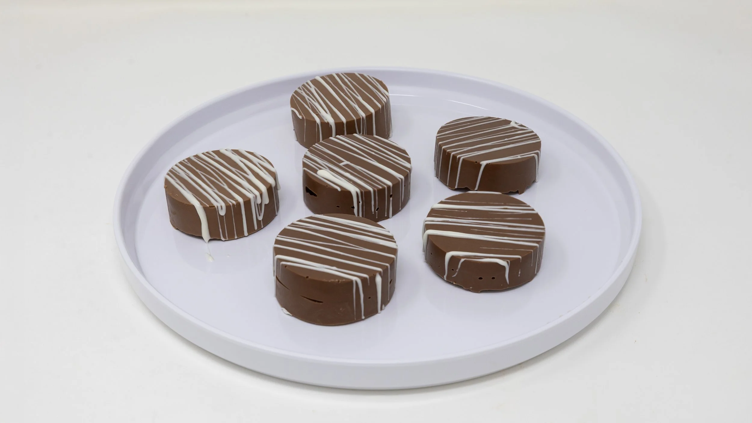 Six round chocolates on a white plate, decorated with white drizzle, on a white background.