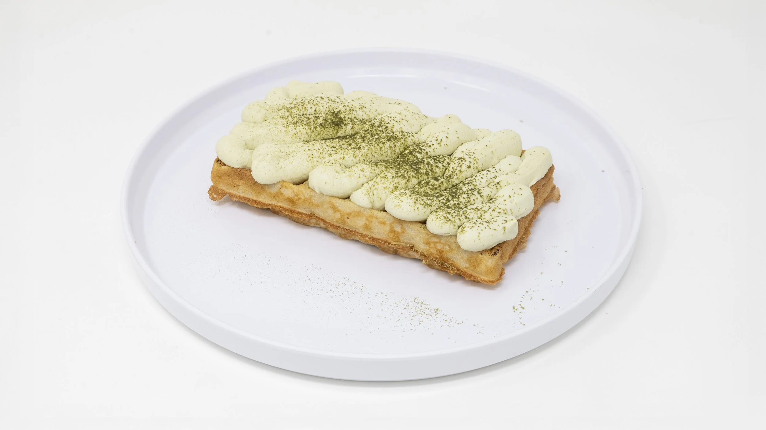 Cream puff pastry topped with whipped cream and green powder on a white plate.