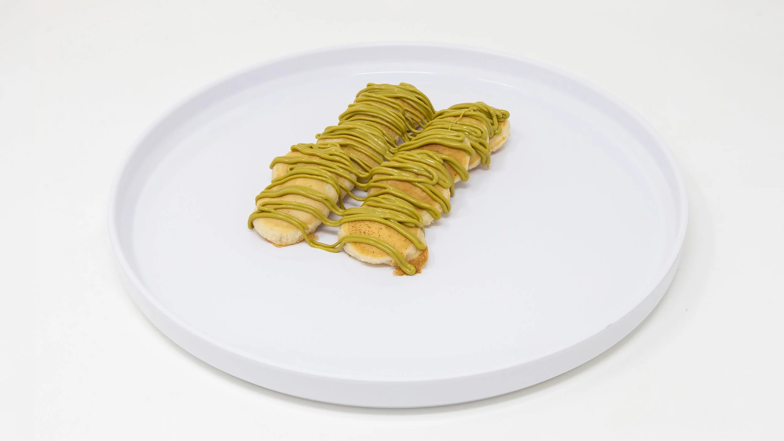 Banana slices topped with matcha-flavored drizzle on a white plate