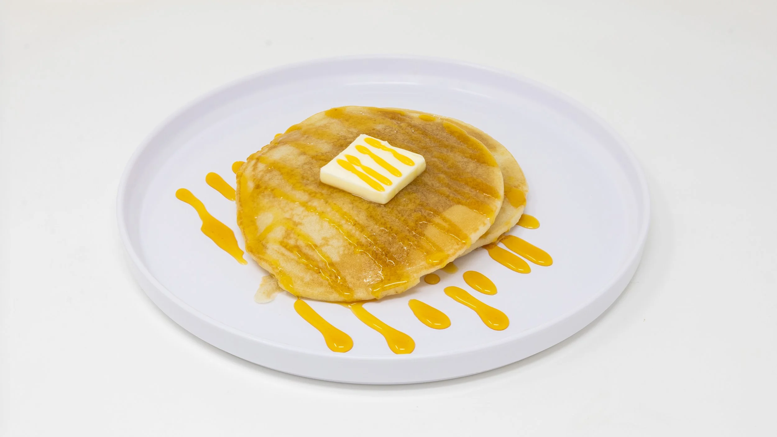 Pancakes with butter and syrup on a white plate