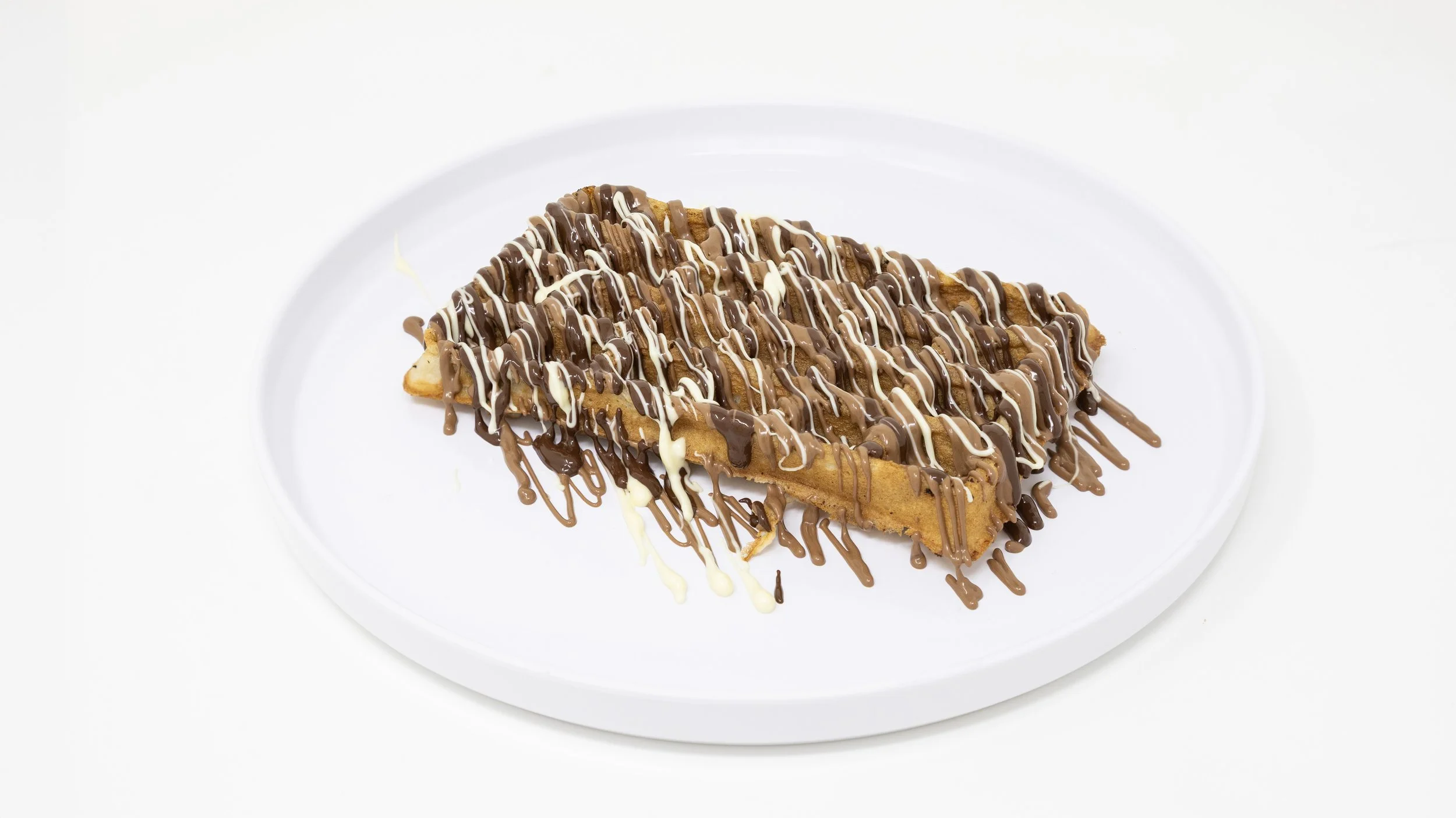 Dessert waffle topped with chocolate and white chocolate drizzle on a white plate
