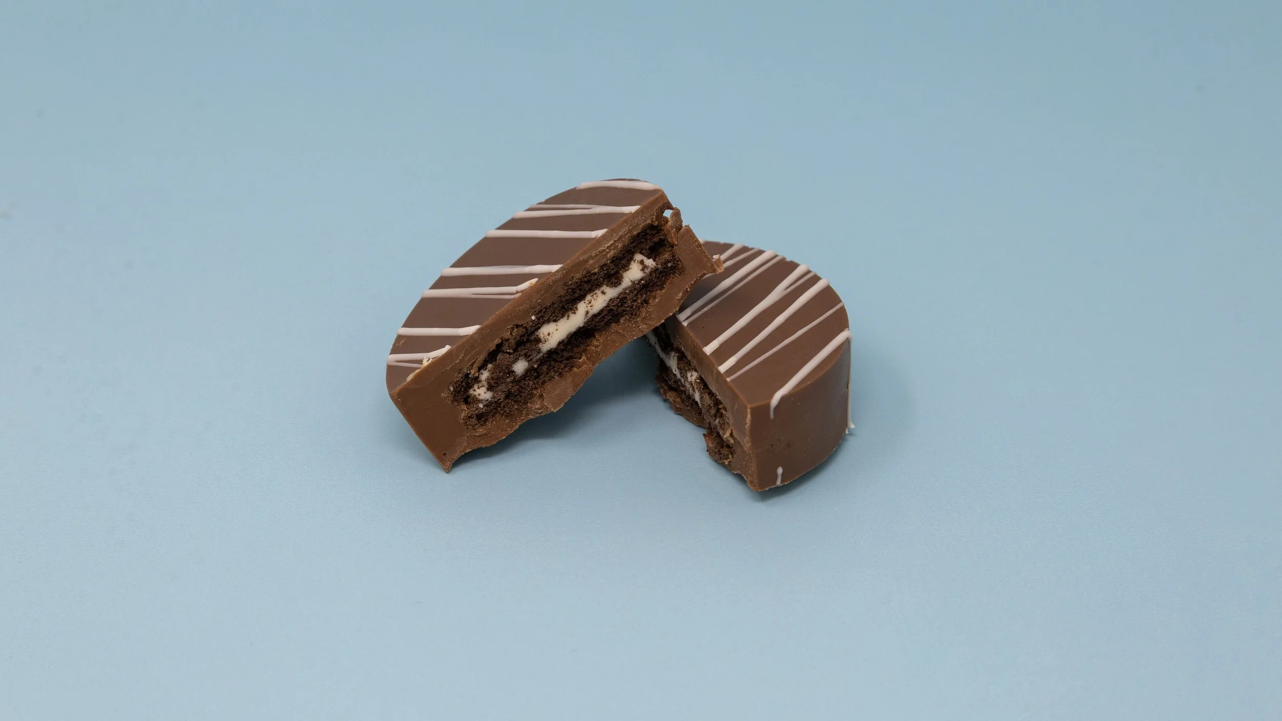Two chocolate cookies with white filling, one broken in half, on a light blue background.