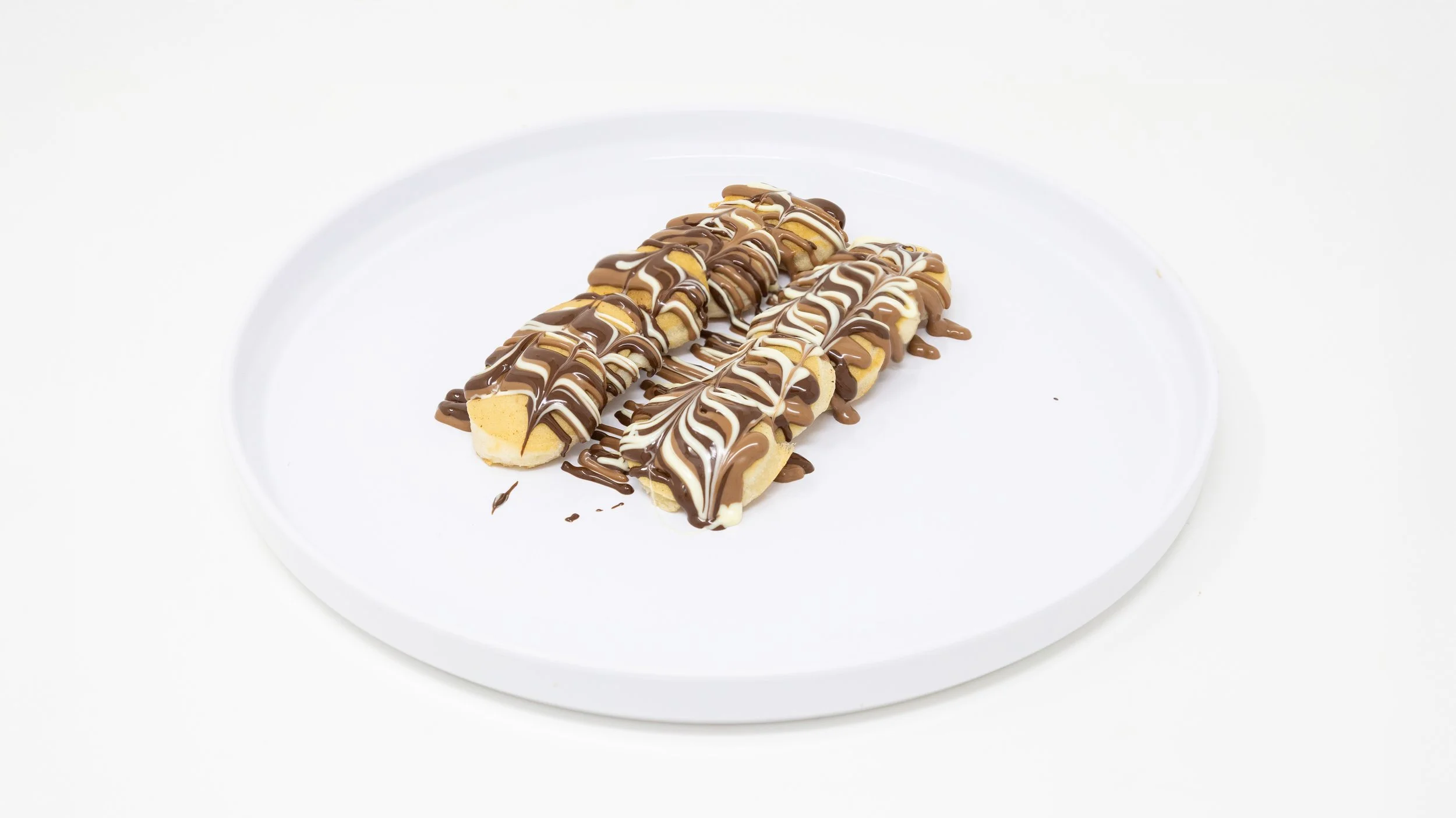 Three chocolate drizzled eclairs on a white plate.