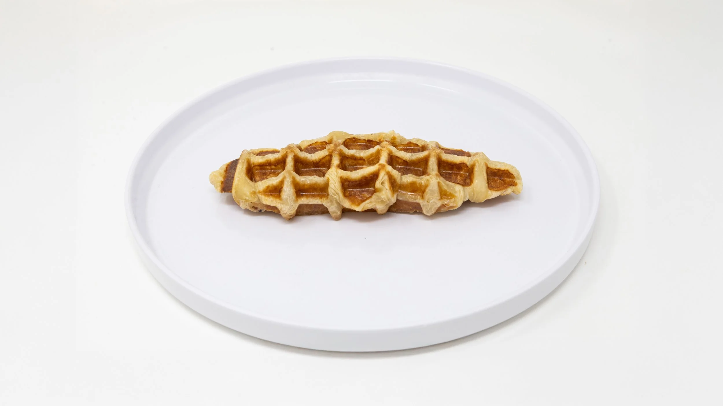 A waffle with a caramel topping on a white plate against a white background.