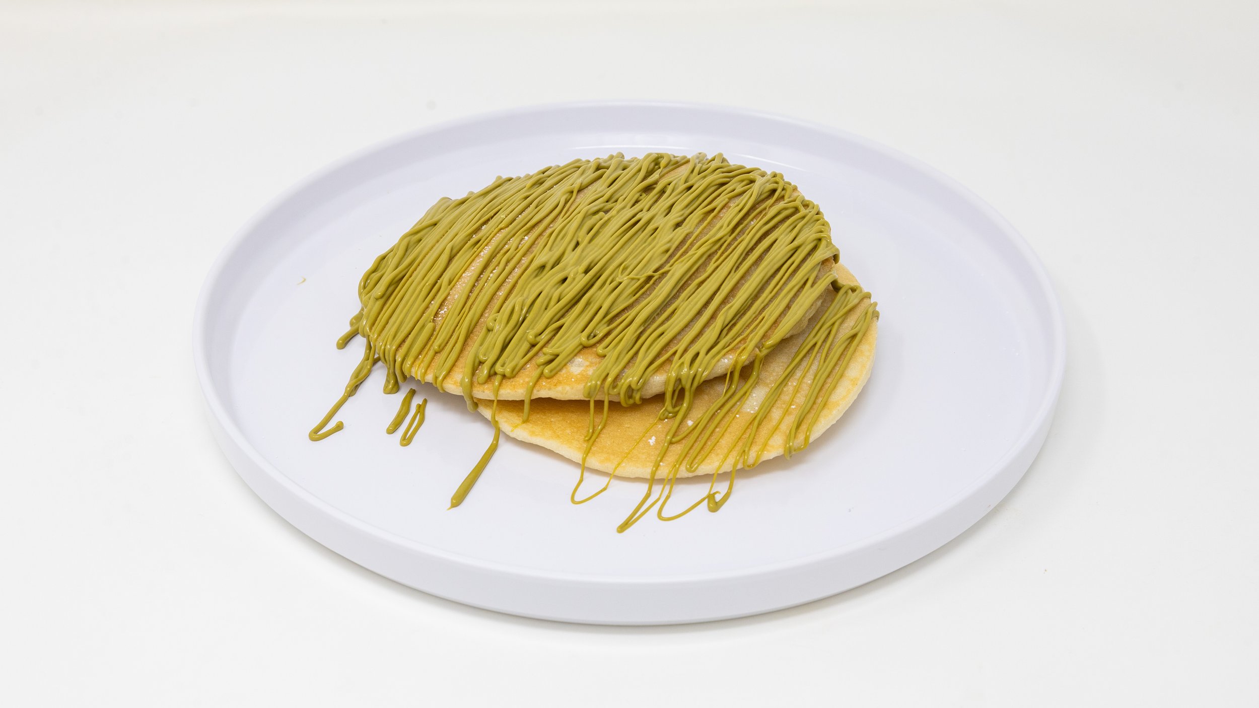A taco shell filled with a folded pancake, topped with green icing or sauce, on a white plate.