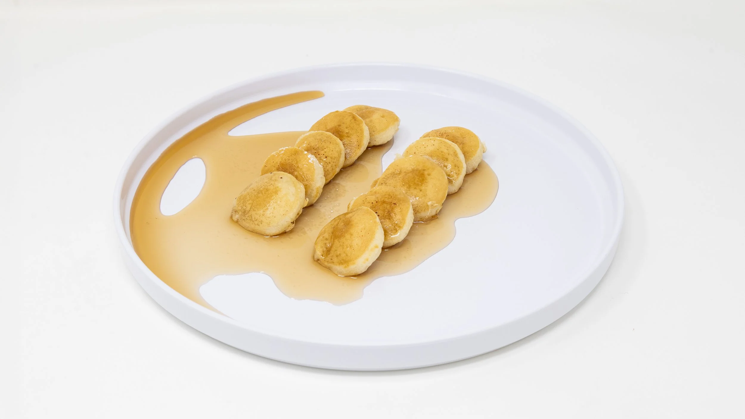 Two rows of sliced bananas drizzled with honey on a white plate against a plain white background.
