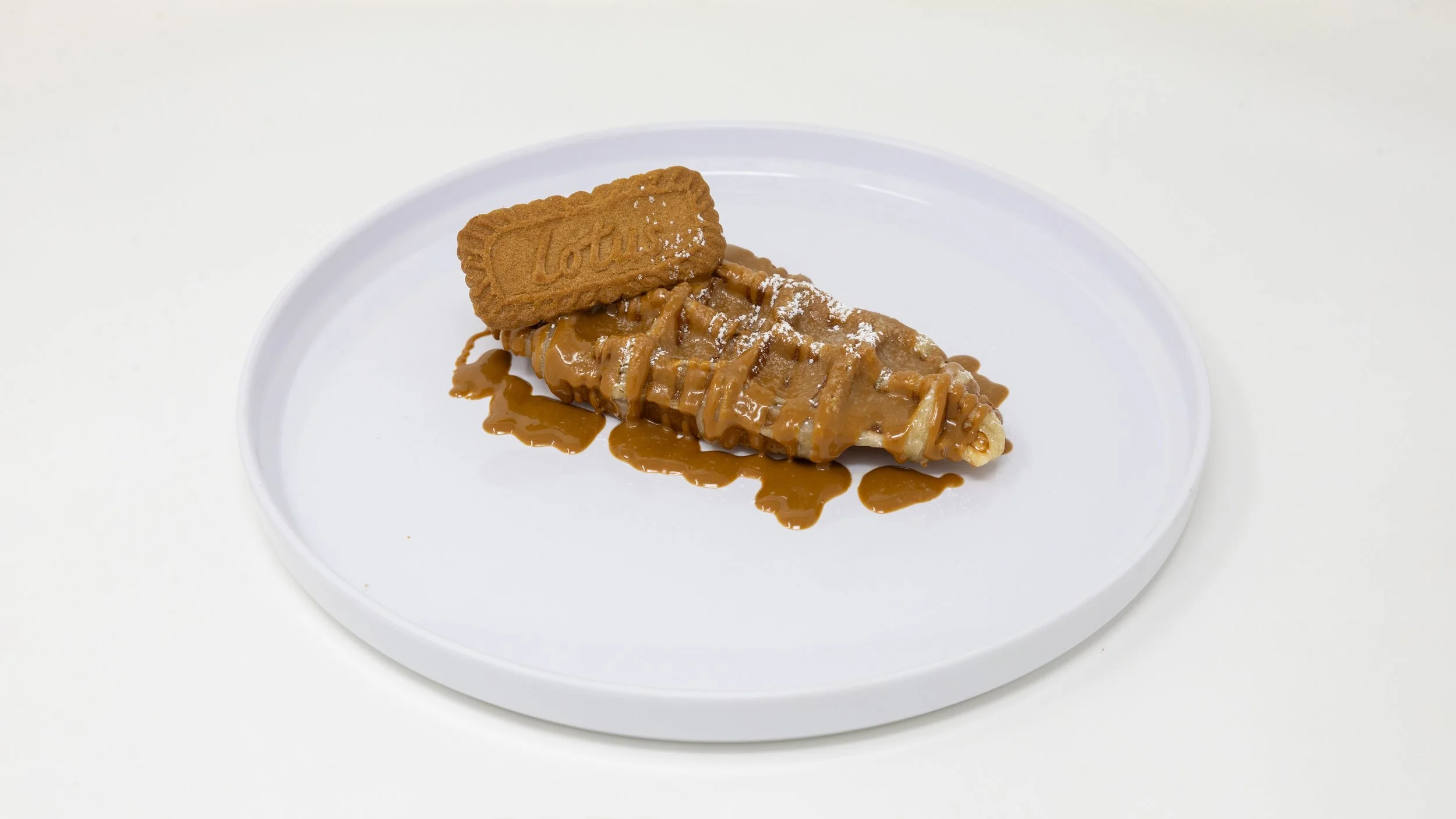 A dessert of fried ice cream drizzled with caramel sauce, topped with a rectangular Lotus biscuit, served on a white plate.