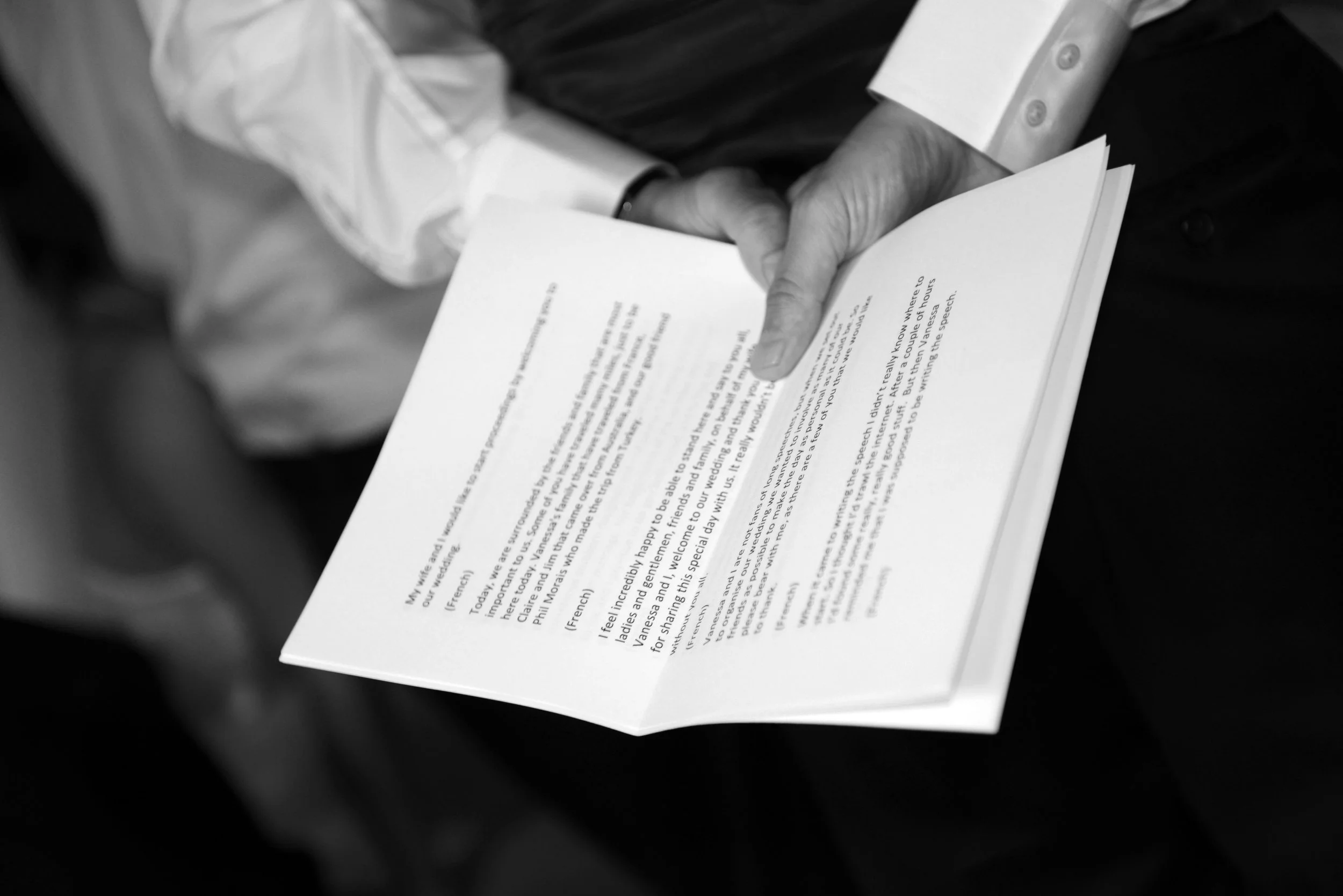 A man in a suit holding an open book or pamphlet in his right hand, with the pages partly folded, in a black and white photo.