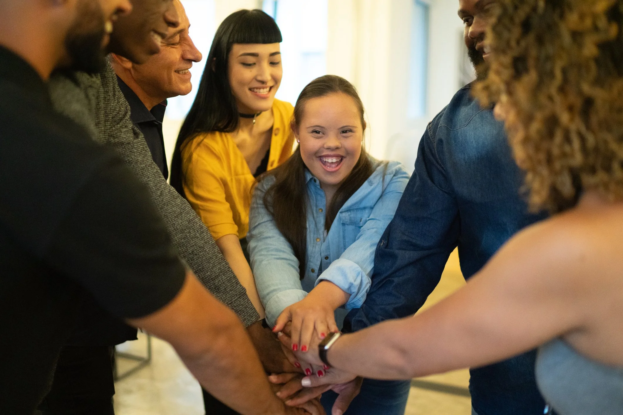 Group of people in a circle with their hands in the middle and a woman with down syndrome looking at camera