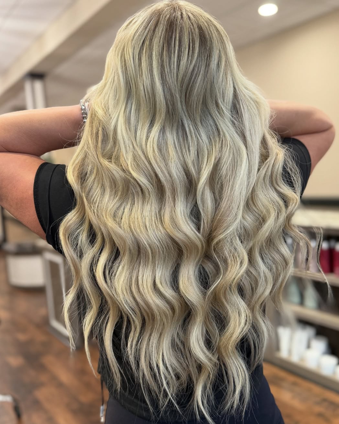 Back view of a woman with long, wavy, blonde hair in a salon setting.